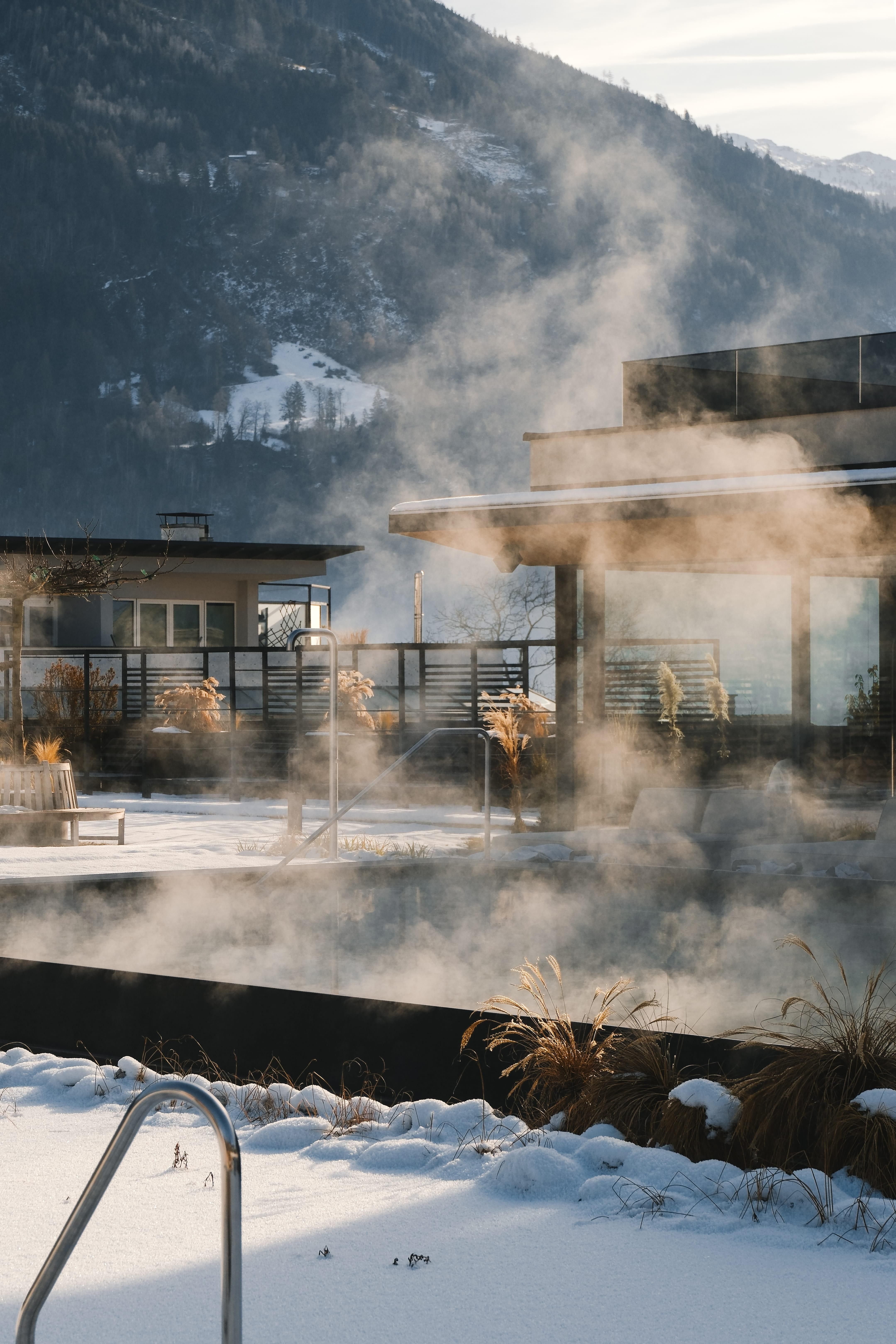 Eine moderne Terrasse mit Dampfwolken und Blick auf die Berge. Der Schnee verleiht der Szene eine ruhige und winterliche Atmosphäre.