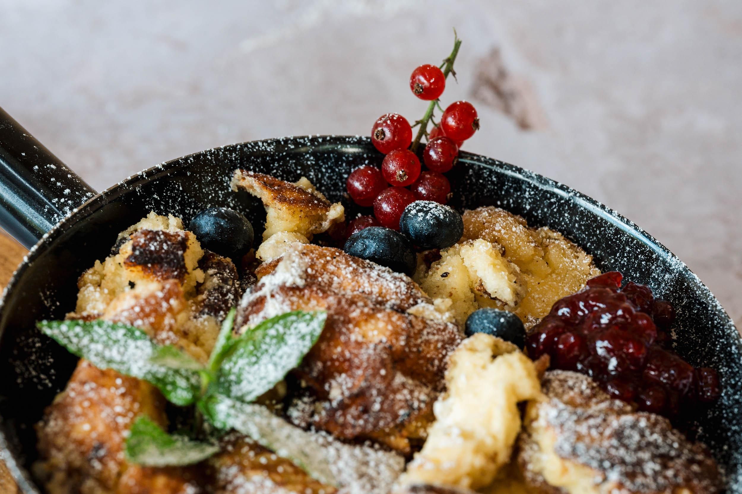 Eine appetitliche Pfanne mit gebackenem Brot, garniert mit Beeren und einem Hauch von Puderzucker. Frische Minze und rote Johannisbeeren ergänzen das Gericht.