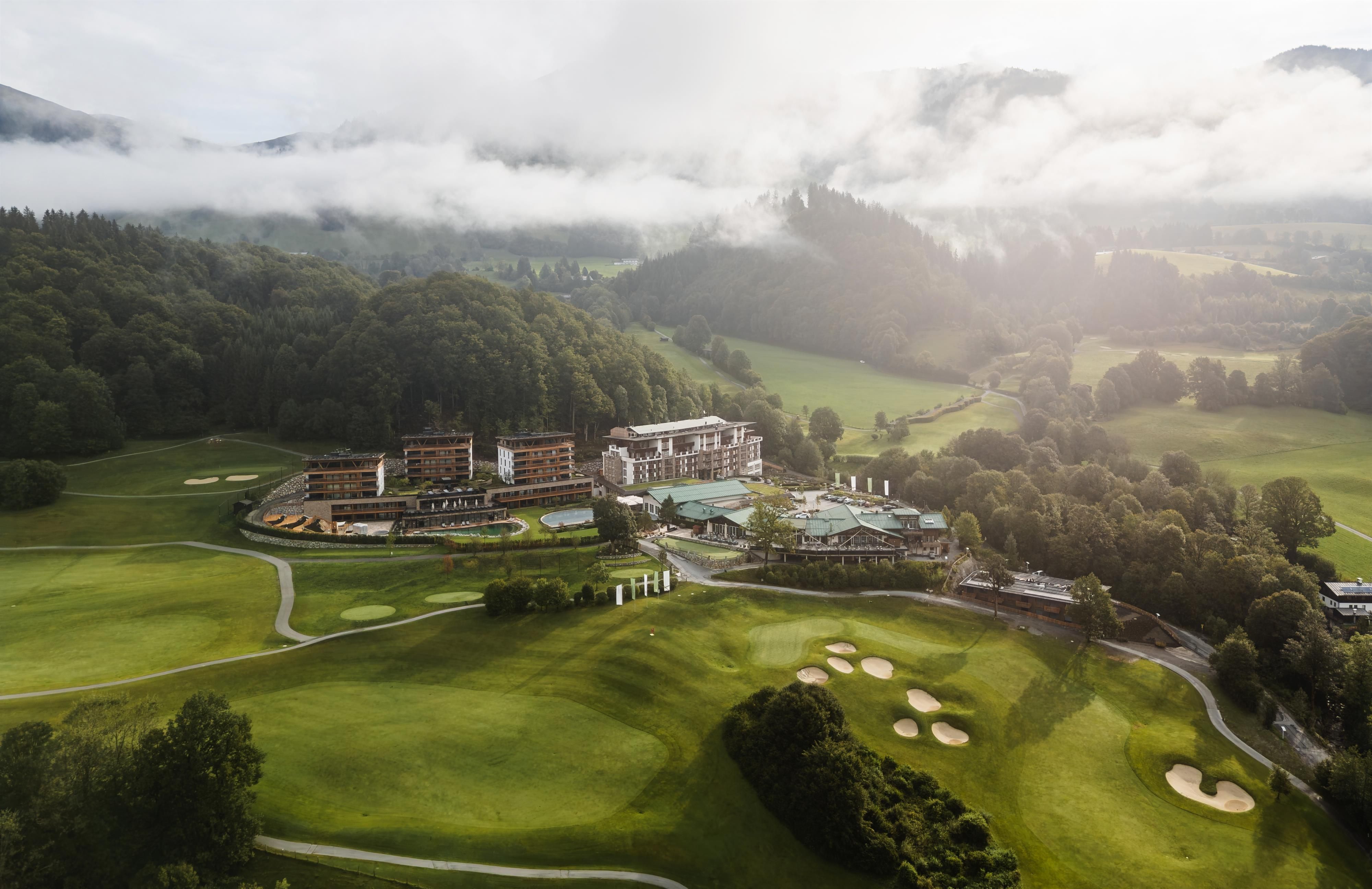 Ein malerisches Golfresort in einer grünen Landschaft mit sanften Hügeln. Der Himmel ist bewölkt, und die Umgebung strahlt Ruhe aus.