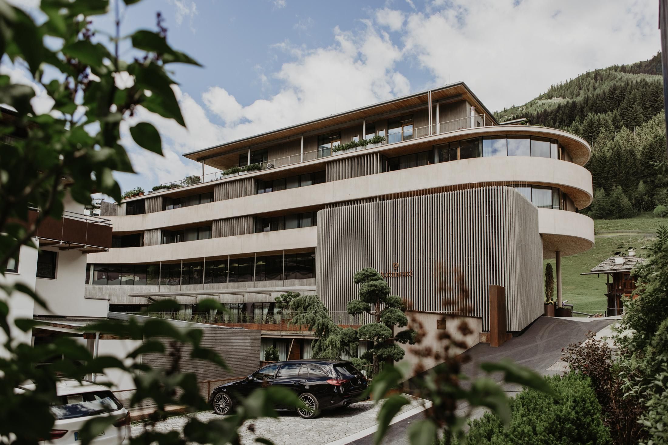Ein modernes Gebäude mit einer geschwungenen Fassade und großen Fenstern. Es ist von grünen Hügeln umgeben und wirkt einladend.