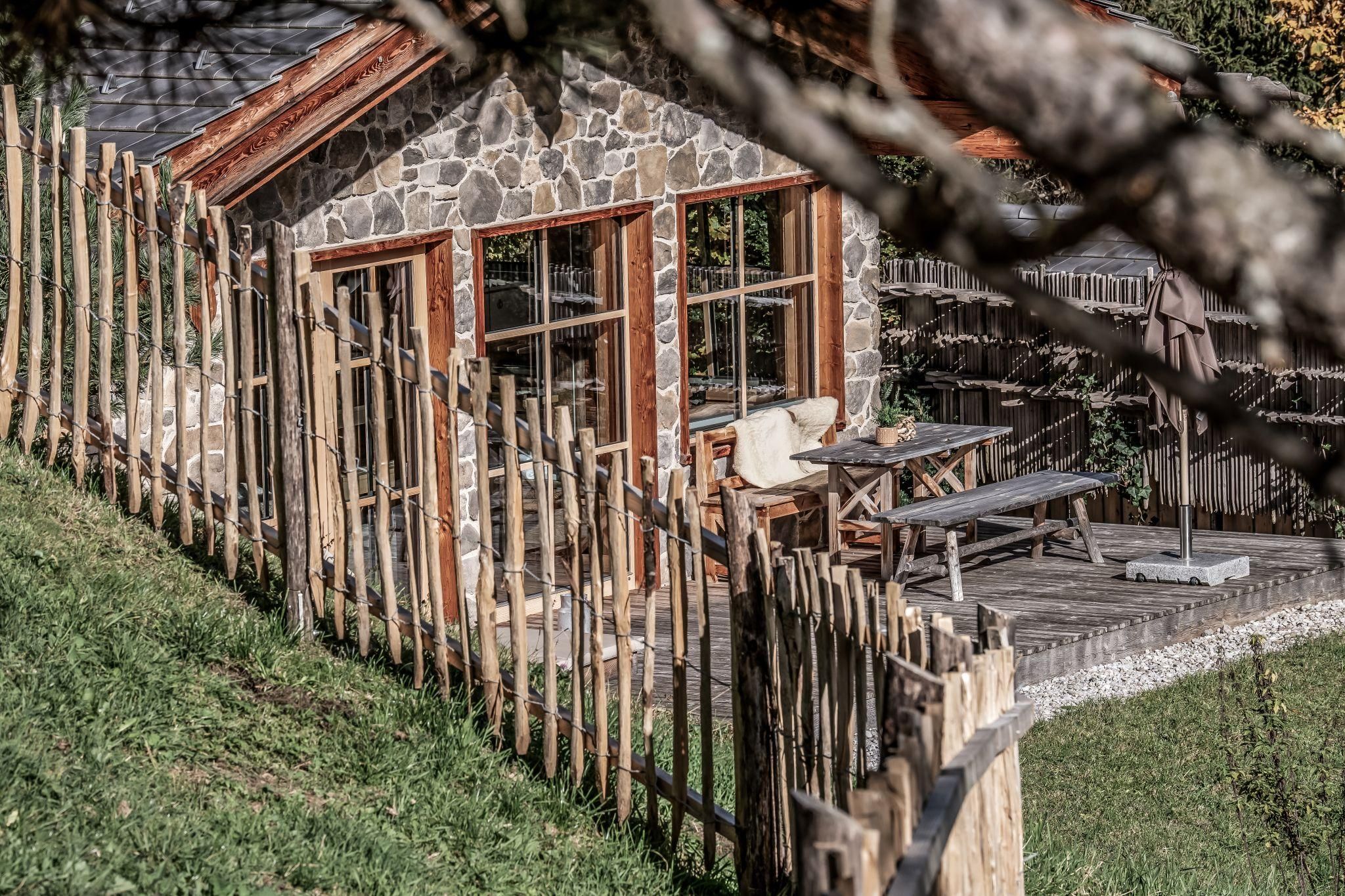 Ein gemütliches Chalet mit großen Fenstern und einer Holzveranda. Es ist von einem niedrigen Zaun und grünem Gras umgeben.