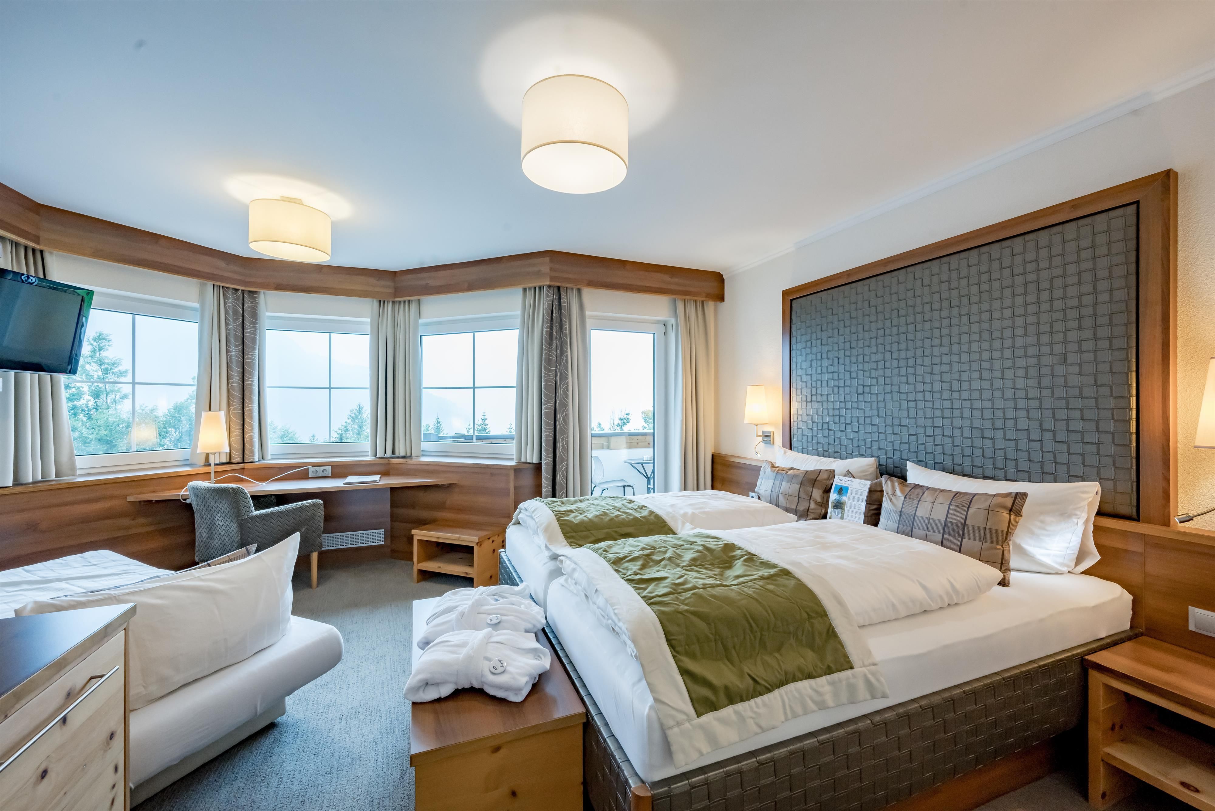 Ein modernes Hotelzimmer mit zwei Betten und einem gemütlichen Sessel. Große Fenster bieten einen Blick auf die Umgebung und sorgen für viel Tageslicht.