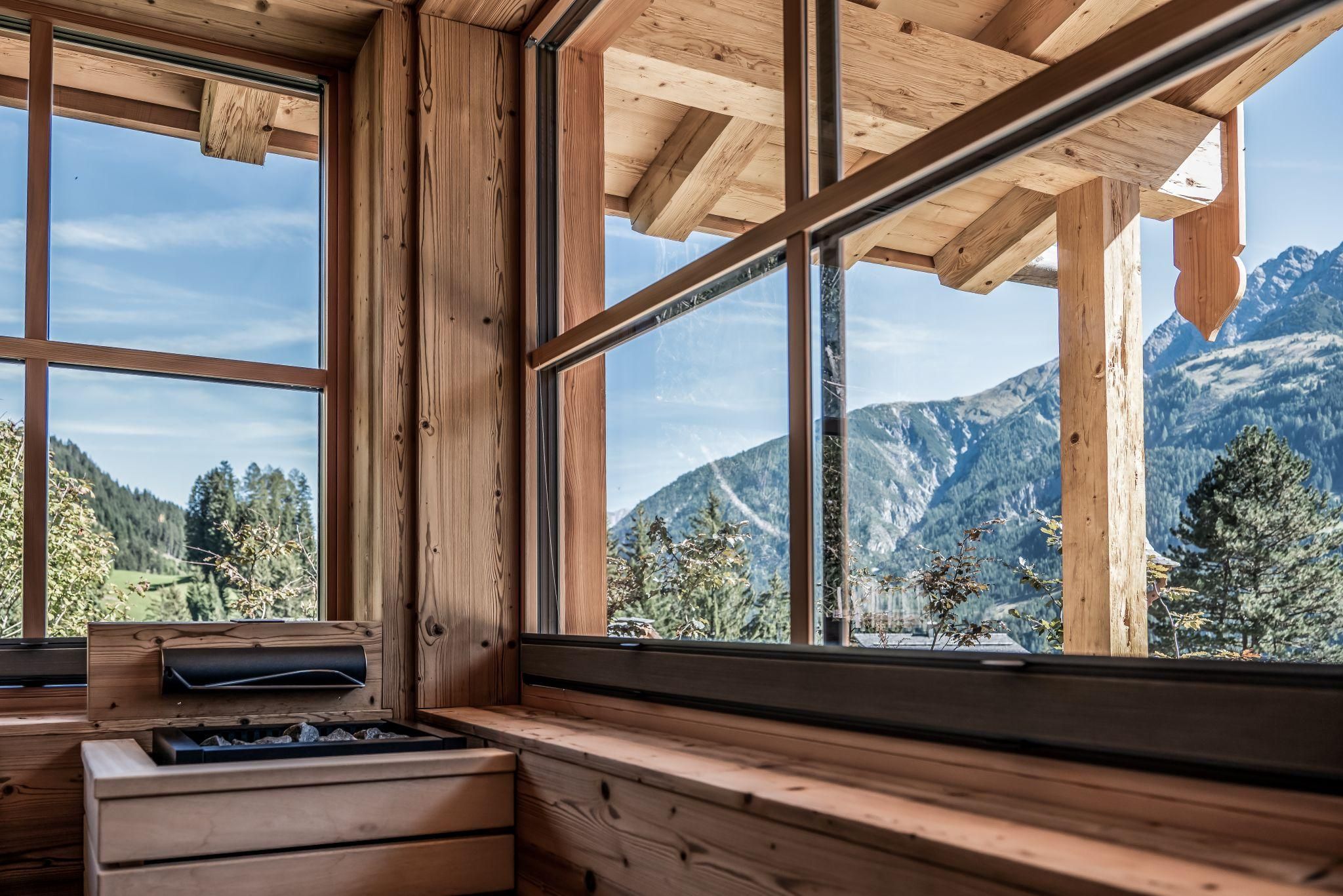 Ein gemütlicher Raum mit großen Fenstern, der einen Blick auf majestätische Berge und einen klaren Himmel bietet. Die Holzverkleidung verleiht eine warme, natürliche Atmosphäre.