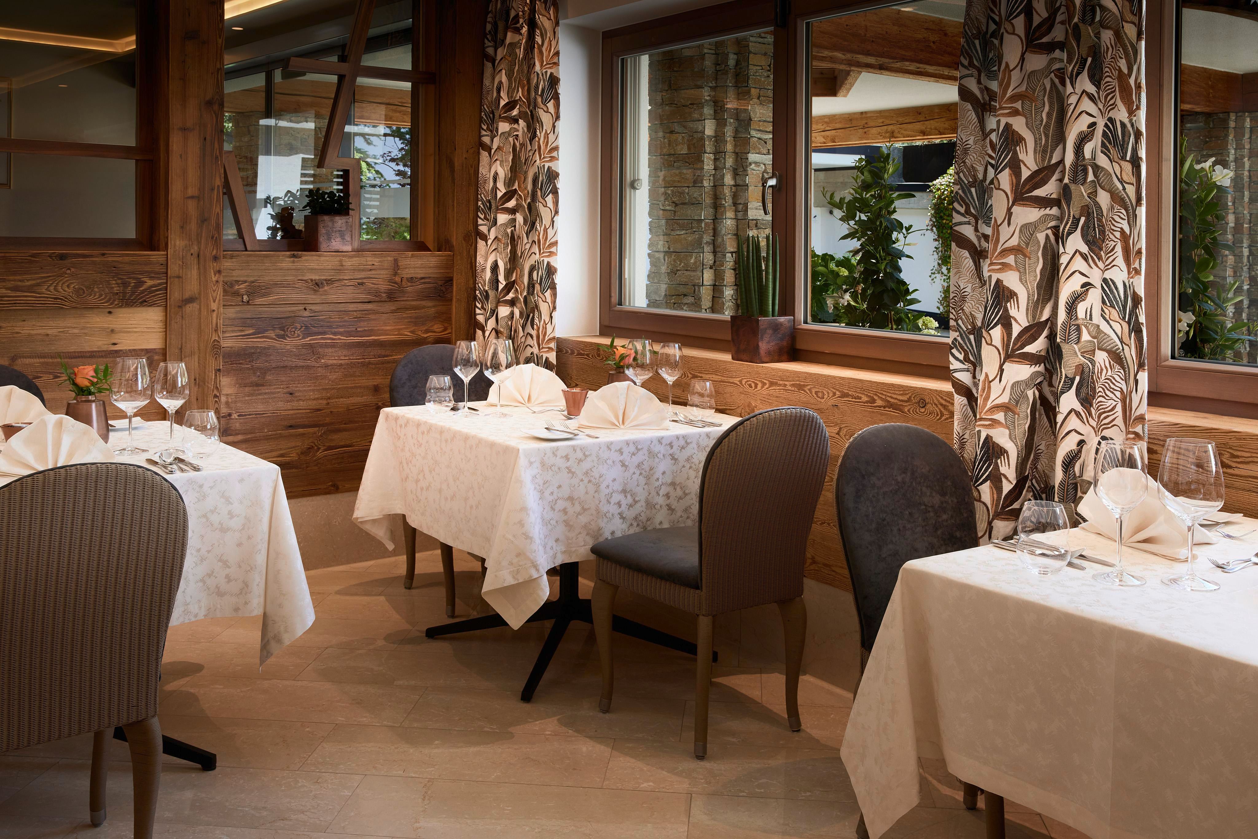 Ein elegantes Restaurant mit dekorierten Tischen und stilvollen Stühlen. Große Fenster sorgen für viel Tageslicht und eine gemütliche Atmosphäre.