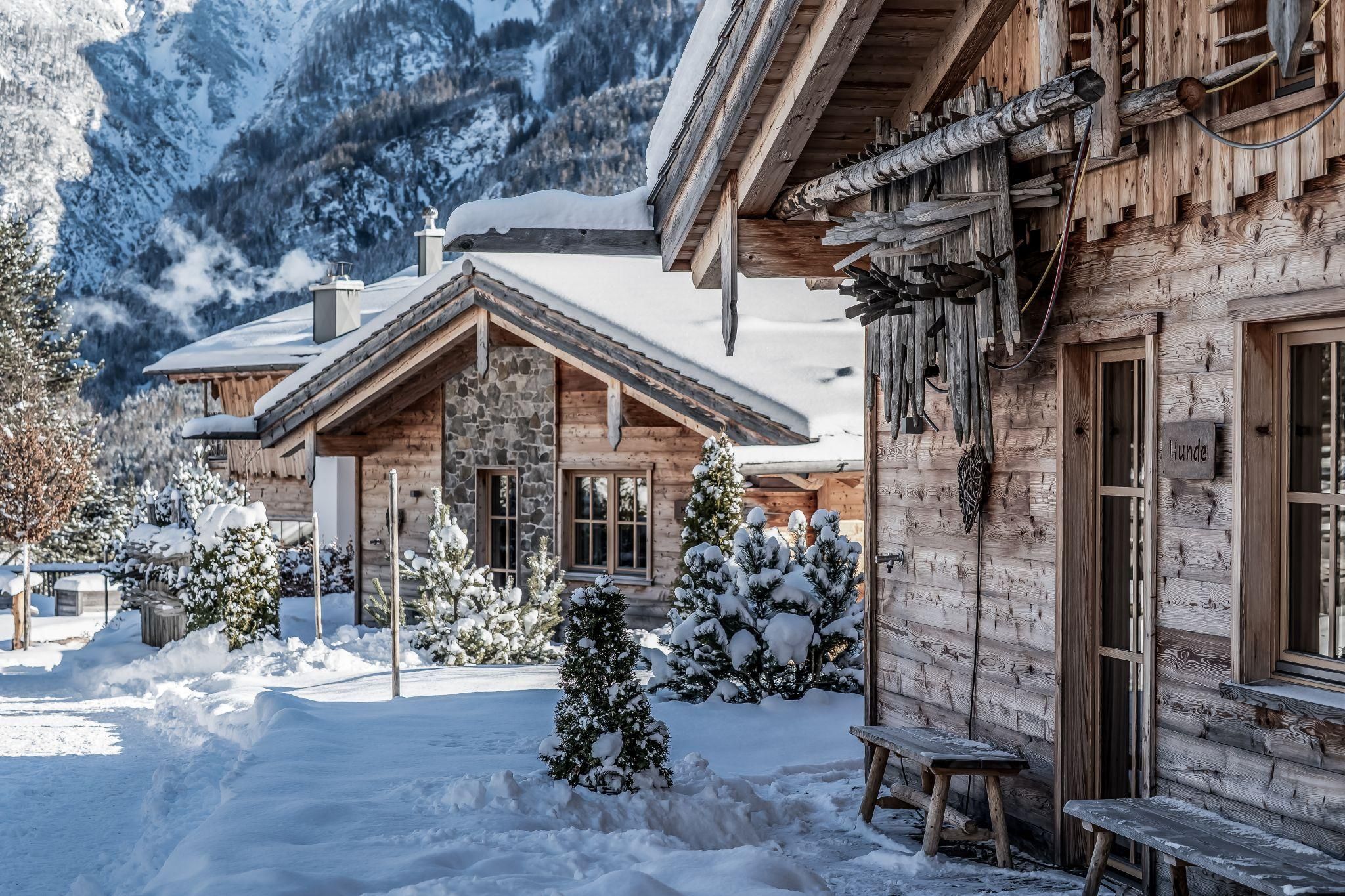 Eine Gruppe von Chalets in einer verschneiten Landschaft. Die Umgebung ist ruhig und malerisch, umgeben von Bergen und Tannenbäumen.