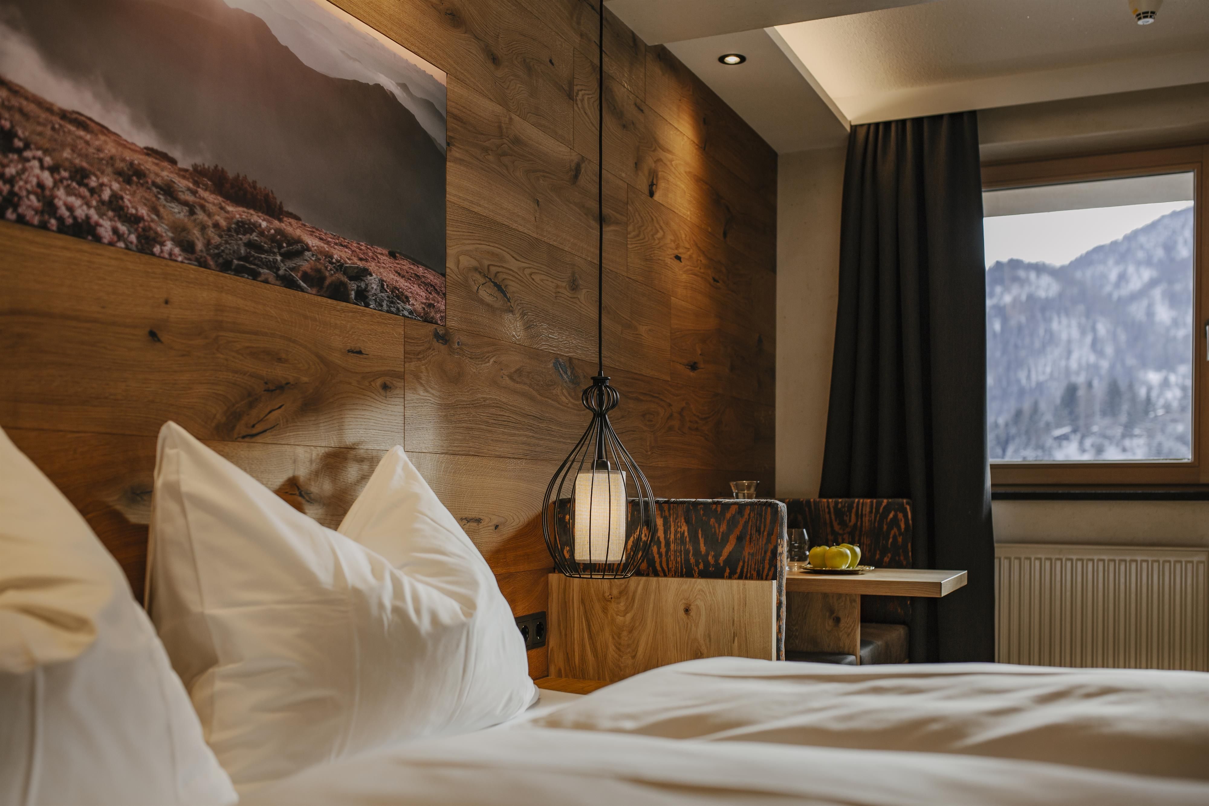 Ein gemütliches Schlafzimmer mit Holzverkleidung und modernen Elementen. Das Fenster bietet einen Blick auf schneebedeckte Berge.