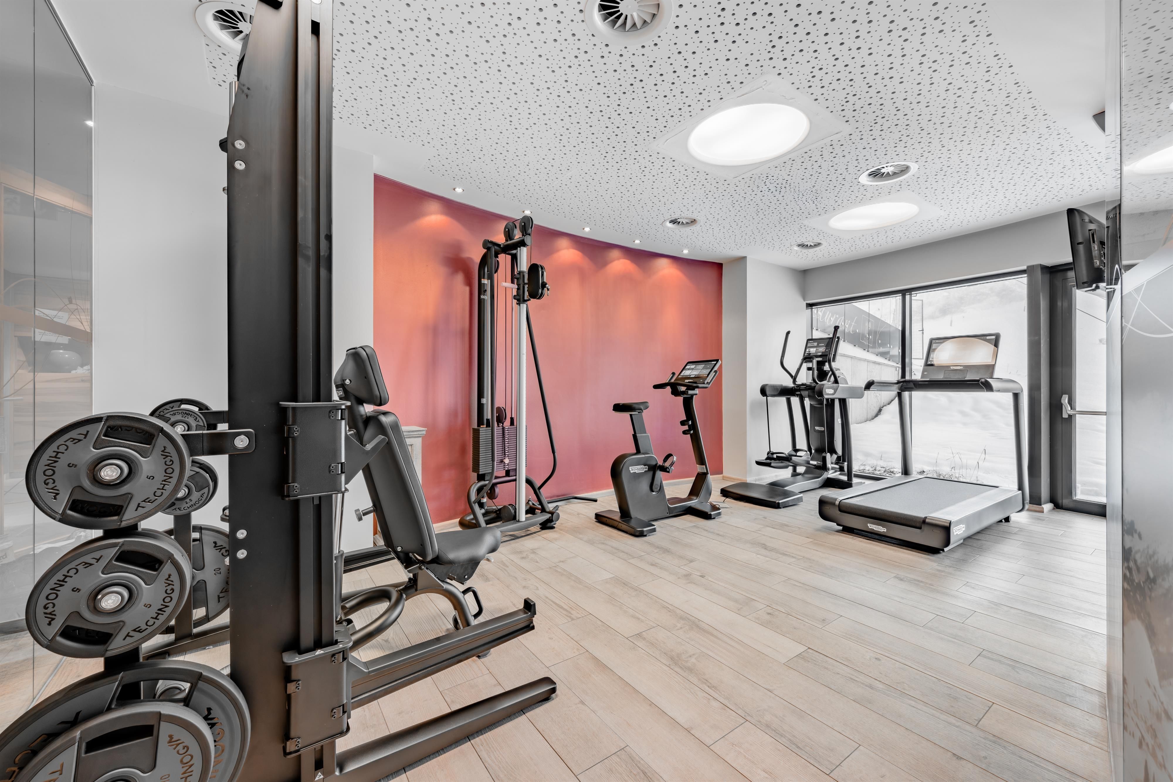 Ein modernes Fitnessstudio mit mehreren Trainingsgeräten. Der Raum ist hell und gut ausgestattet mit Holzfußboden.