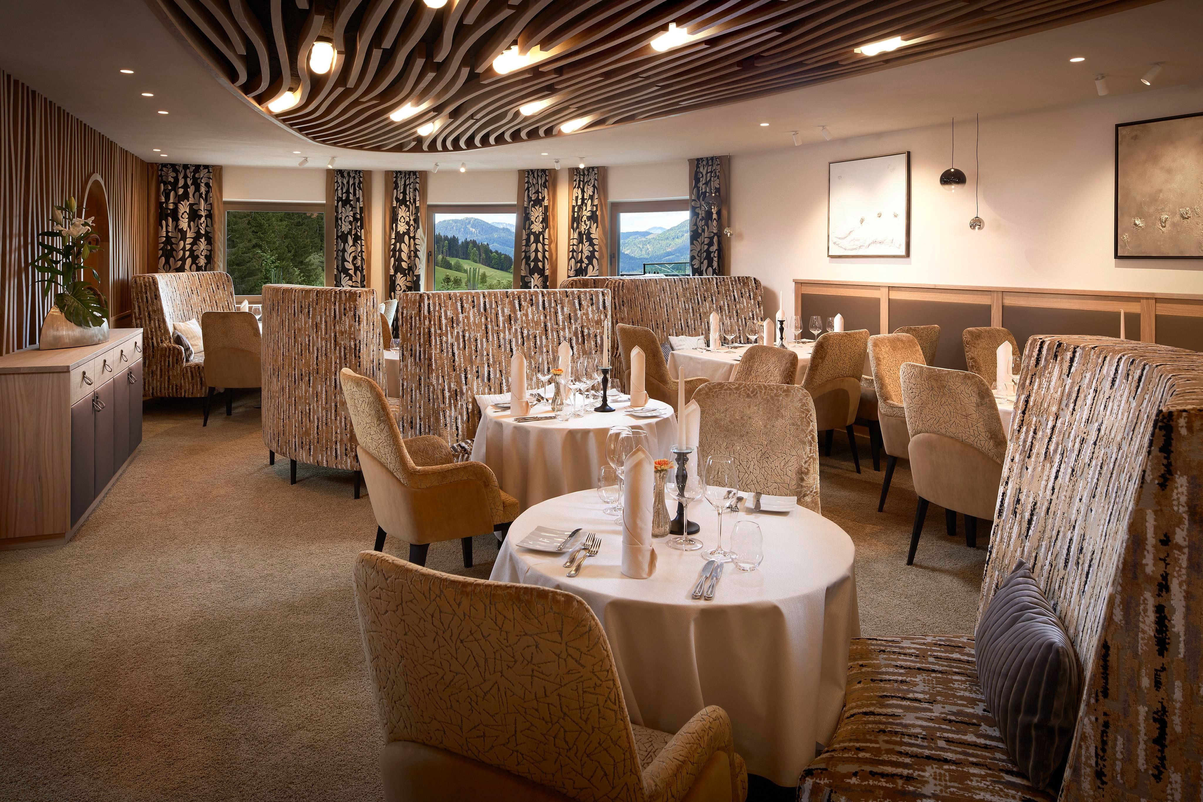 Ein elegantes Restaurant mit gemütlichen Tischen und Stühlen. Große Fenster bieten einen Blick auf die grüne Landschaft.