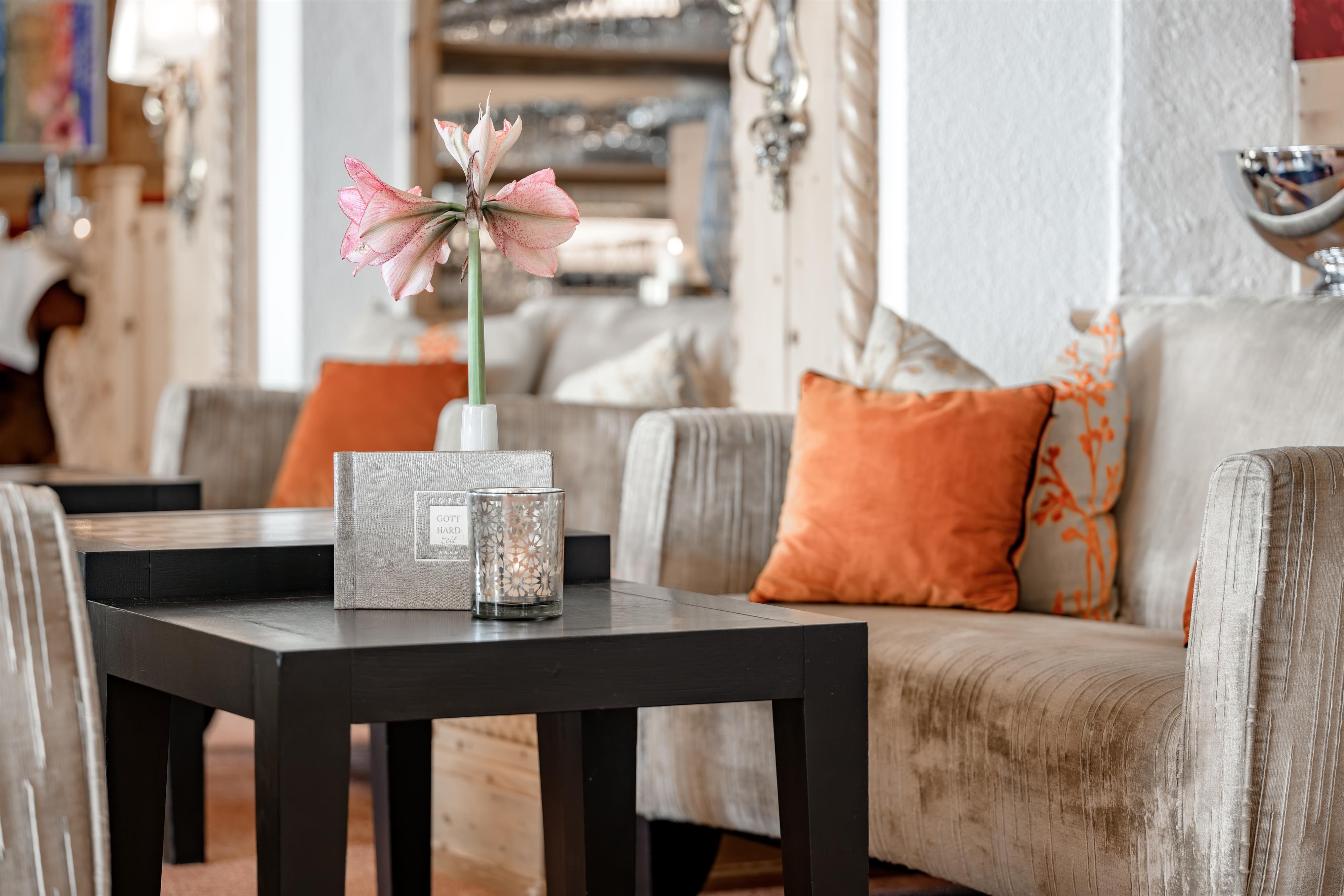 Ein eleganter Wohnbereich mit bequemen Sofas und farbigen Kissen. Auf einem schwarzen Tisch steht eine Vase mit einer schönen Blume.