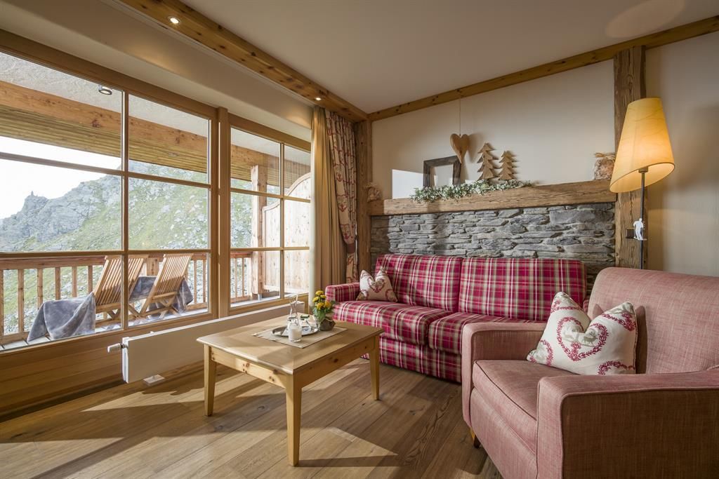 Ein gemütliches Wohnzimmer mit einem karierten Sofa und einem harmonischen Holztouch. Große Fenster bieten einen Blick auf die Berglandschaft.