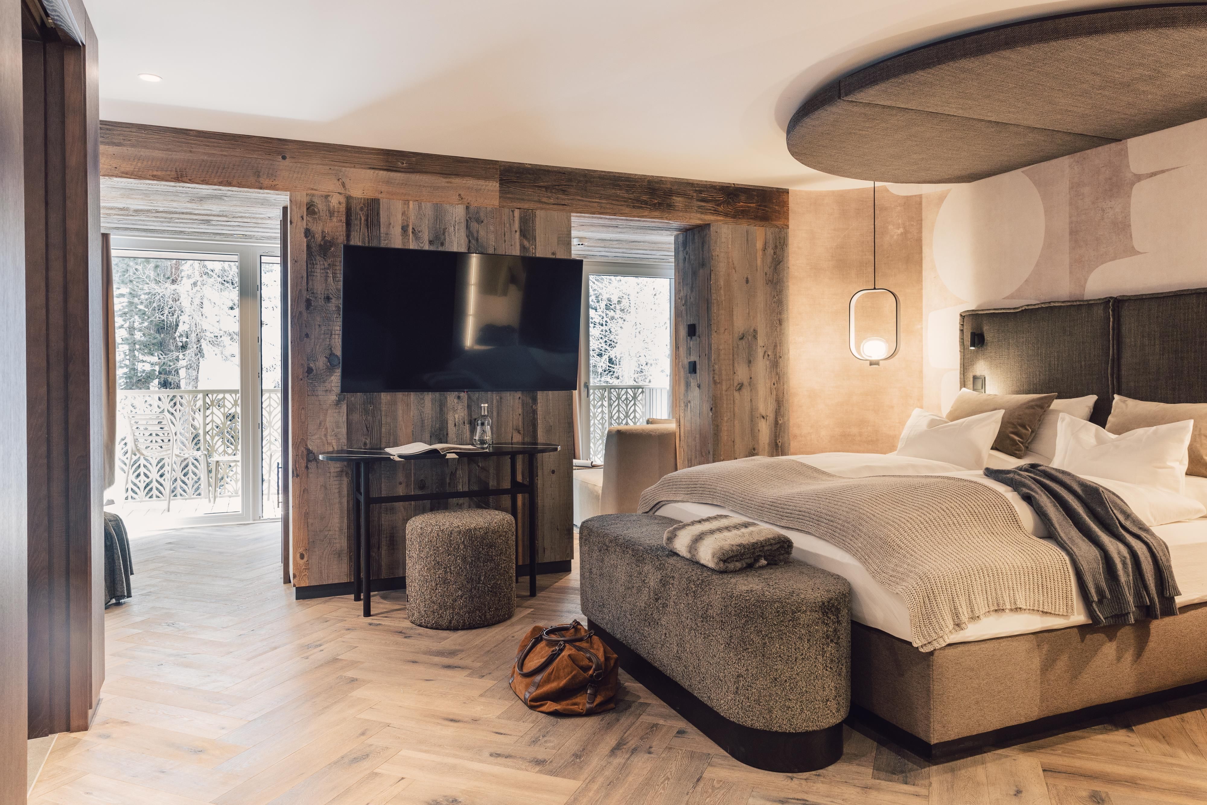 Ein modernes Schlafzimmer mit einem großen Bett und einem Flachbildfernseher. Der Raum hat Holzverkleidung und große Fenster, die viel Licht hereinlassen.