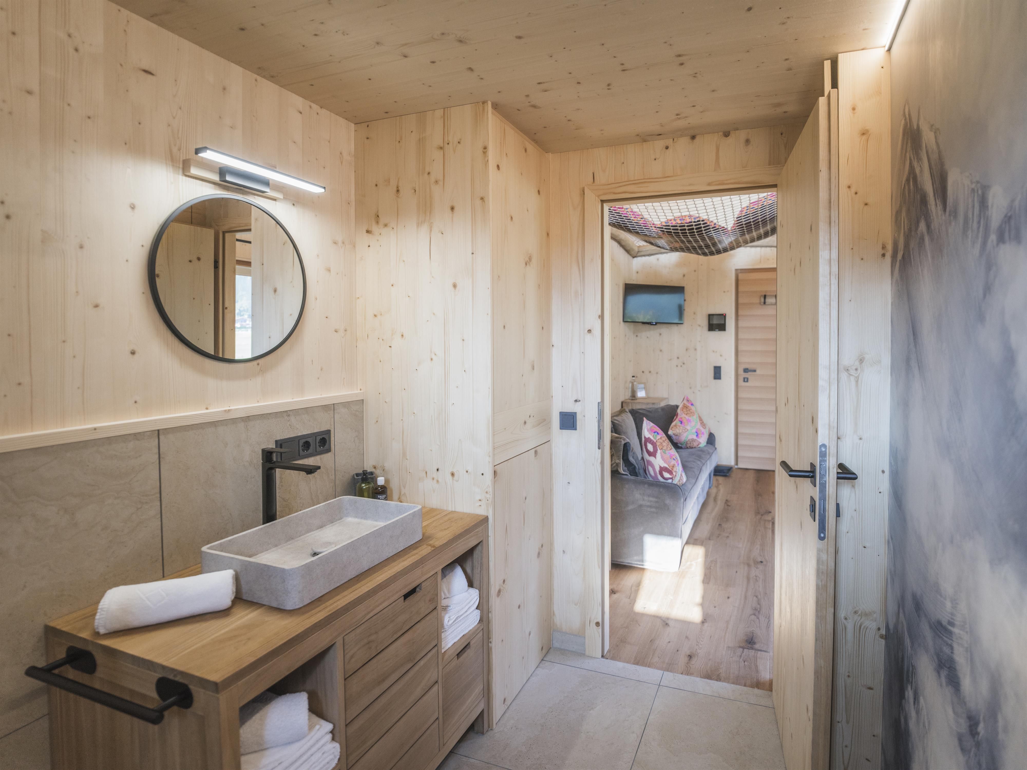 Ein modernes Badezimmer mit Holzverkleidung und einem Waschbecken. Ein Spiegel und frische Handtücher sorgen für eine einladende Atmosphäre.