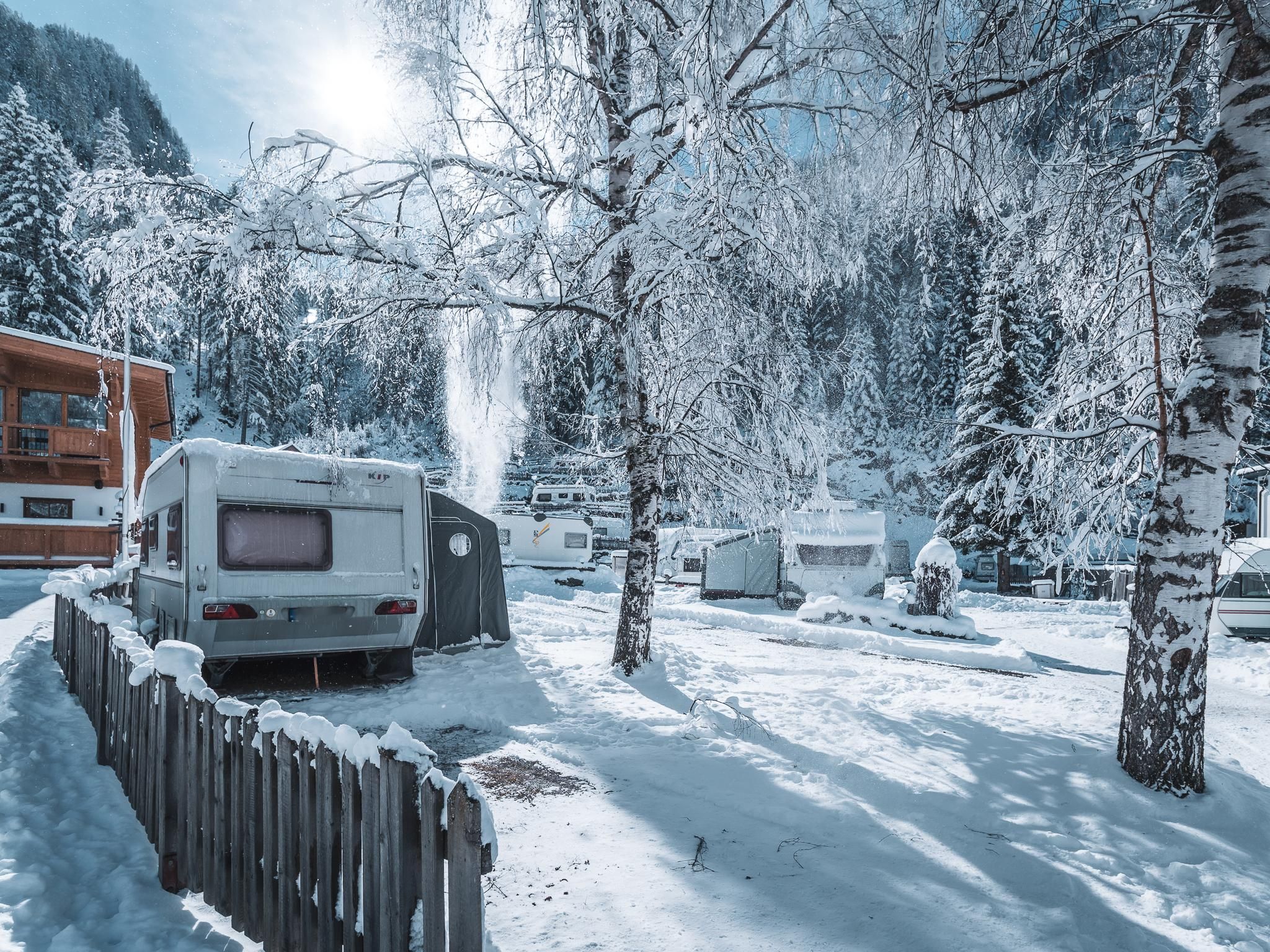 Ein winterlicher Campingplatz mit Wohnwagen und schneebedeckten Bäumen. Die Landschaft ist ruhig und von frostigem Glanz geprägt.