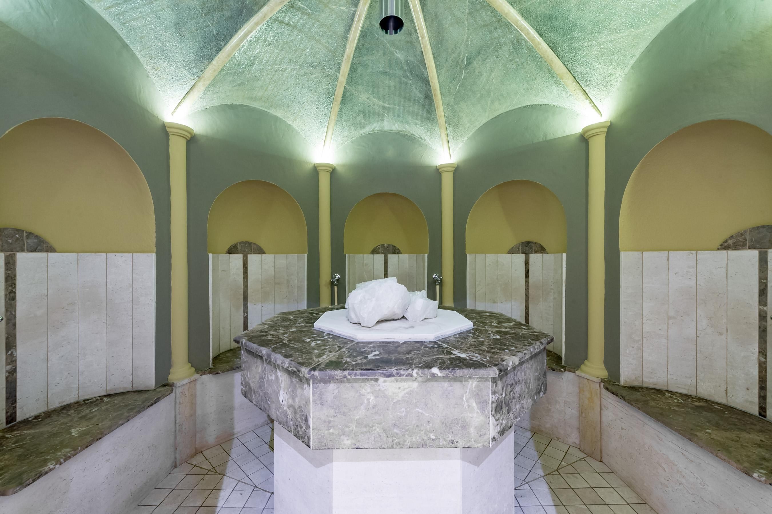 Ein stilvolles Badehaus mit einem zentralen Marmortisch. Die Wände sind in dezenten Farben gehalten und die Beleuchtung schafft eine entspannende Atmosphäre.