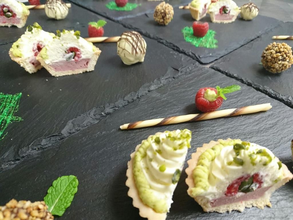 Ein kunstvoll angerichtetes Dessert-Tableau mit verschiedenen süßen Köstlichkeiten. Die Platten enthalten kleine Törtchen, Pralinen und frische Beeren.