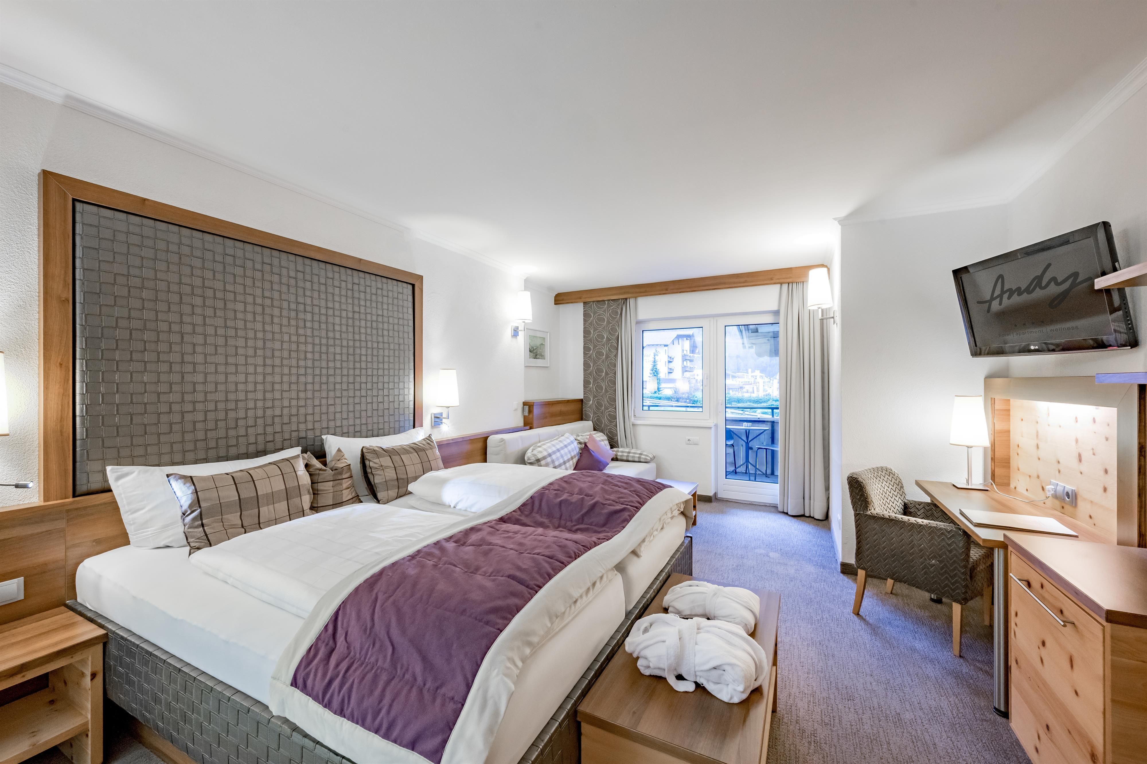 Ein modernes Hotelzimmer mit einem großen Bett und Holzdetails. Der Raum verfügt über einen Schreibtisch und einen Balkon mit Blick nach draußen.