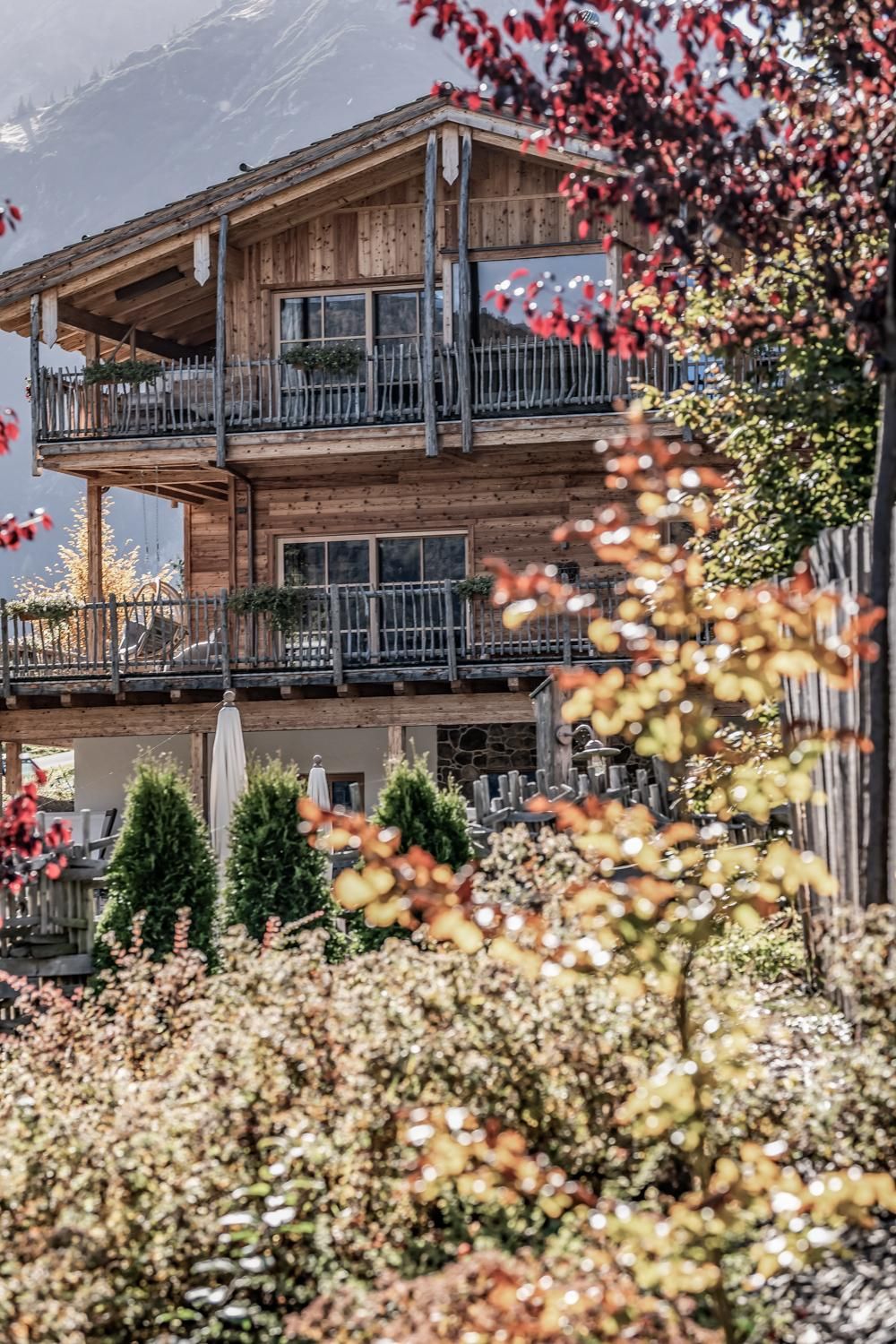 Ein schönes Chalet mit mehreren Balkonen und einem gepflegten Garten. Bunte Pflanzen und Bäume umgeben die Unterkunft und schaffen eine einladende Atmosphäre.