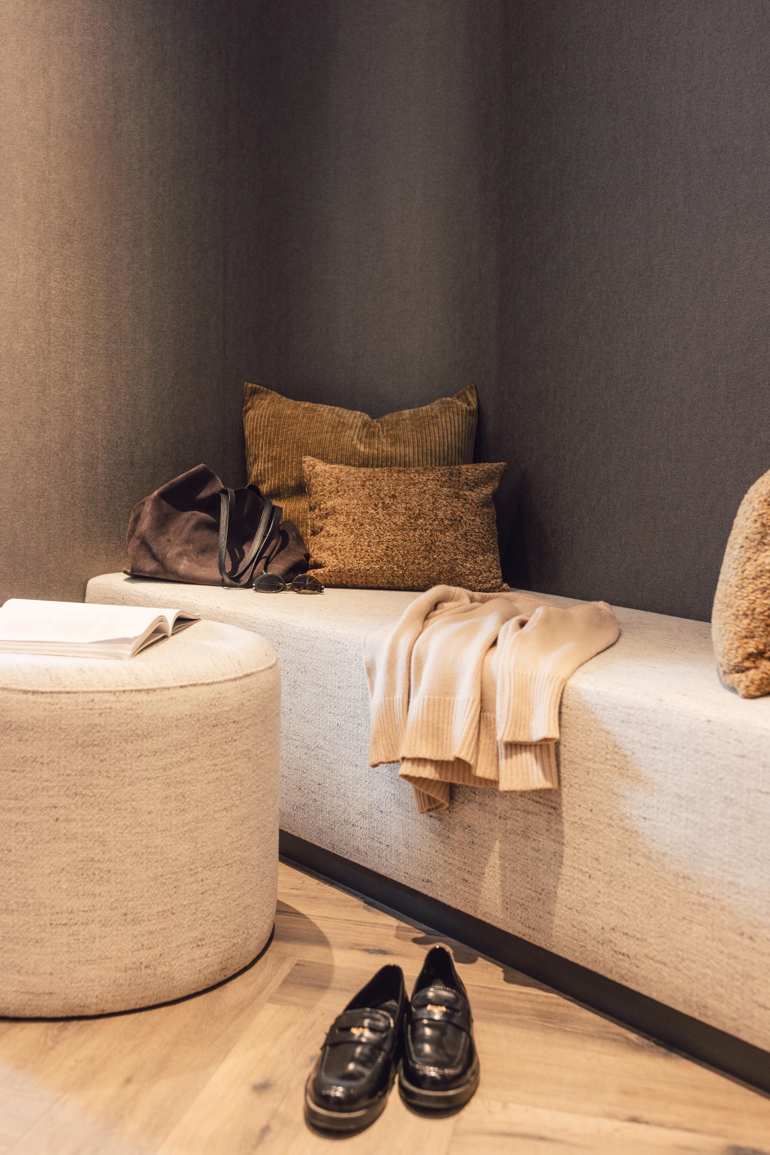 Ein stilvoller Innenraum mit einer bequemen Bank und dekorativen Kissen. Neben der Bank liegt eine Jacke und ein Paar elegante Schuhe.