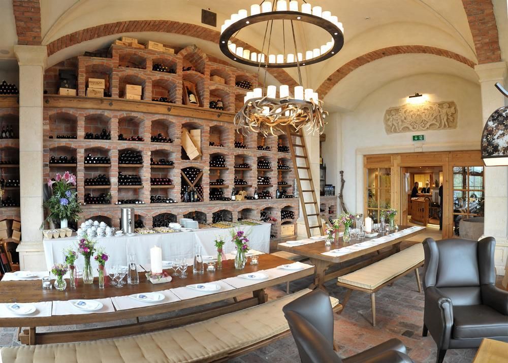 Ein stilvolles Restaurant mit einer Wand aus Weinregalen und einem langen Tisch. Die Einrichtung ist gemütlich und einladend, ideal für Abendessen.