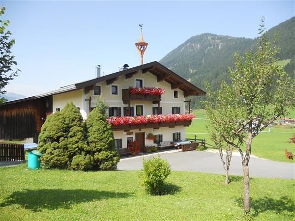 Ein traditionelles Haus mit Blumenkästen und einem schönen Garten. Im Hintergrund sind sanfte Berge zu sehen.
