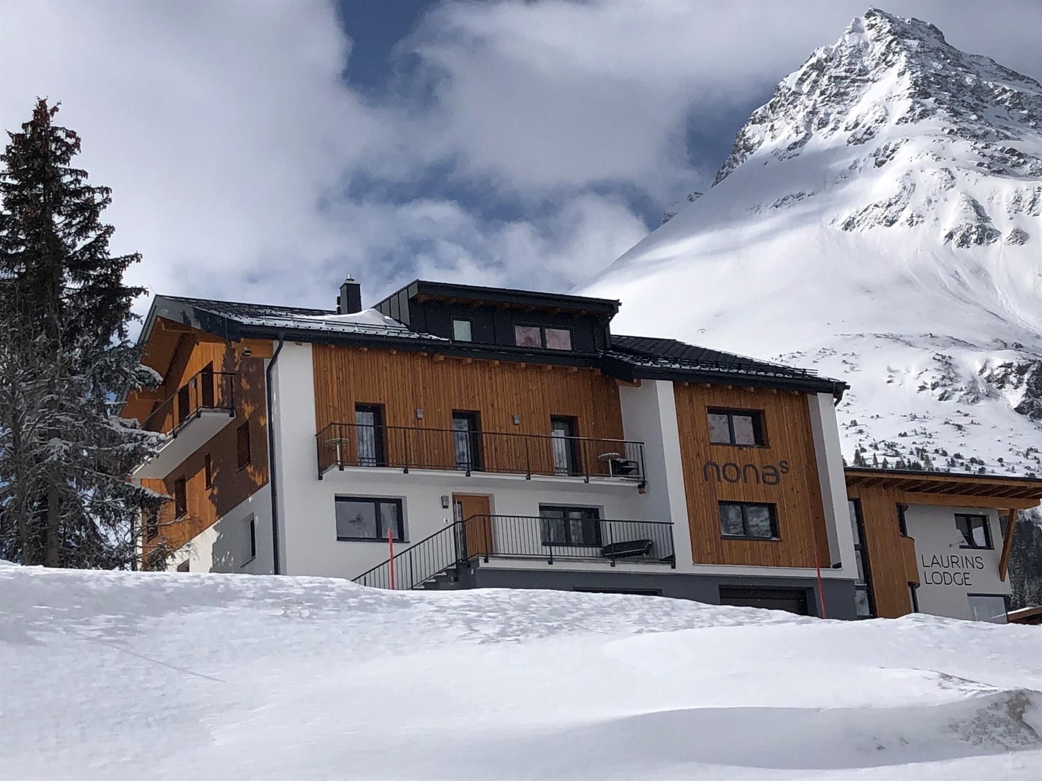 Ein charmantes Berghaus im Schnee, umgeben von hohen Bergen. Der Himmel ist bewölkt und verleiht der Szenerie eine ruhige Atmosphäre.