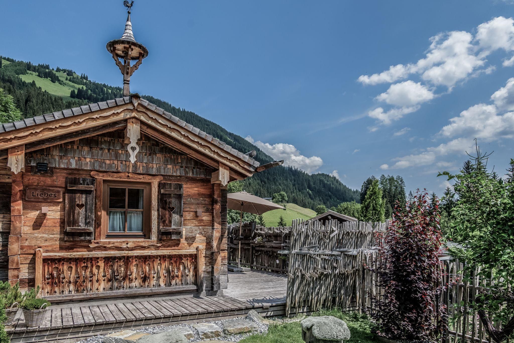 Ein traditionelles Chalet umgeben von grünen Hügeln und blauen Himmel. Die gemütliche Atmosphäre wird durch die umliegende Natur verstärkt.