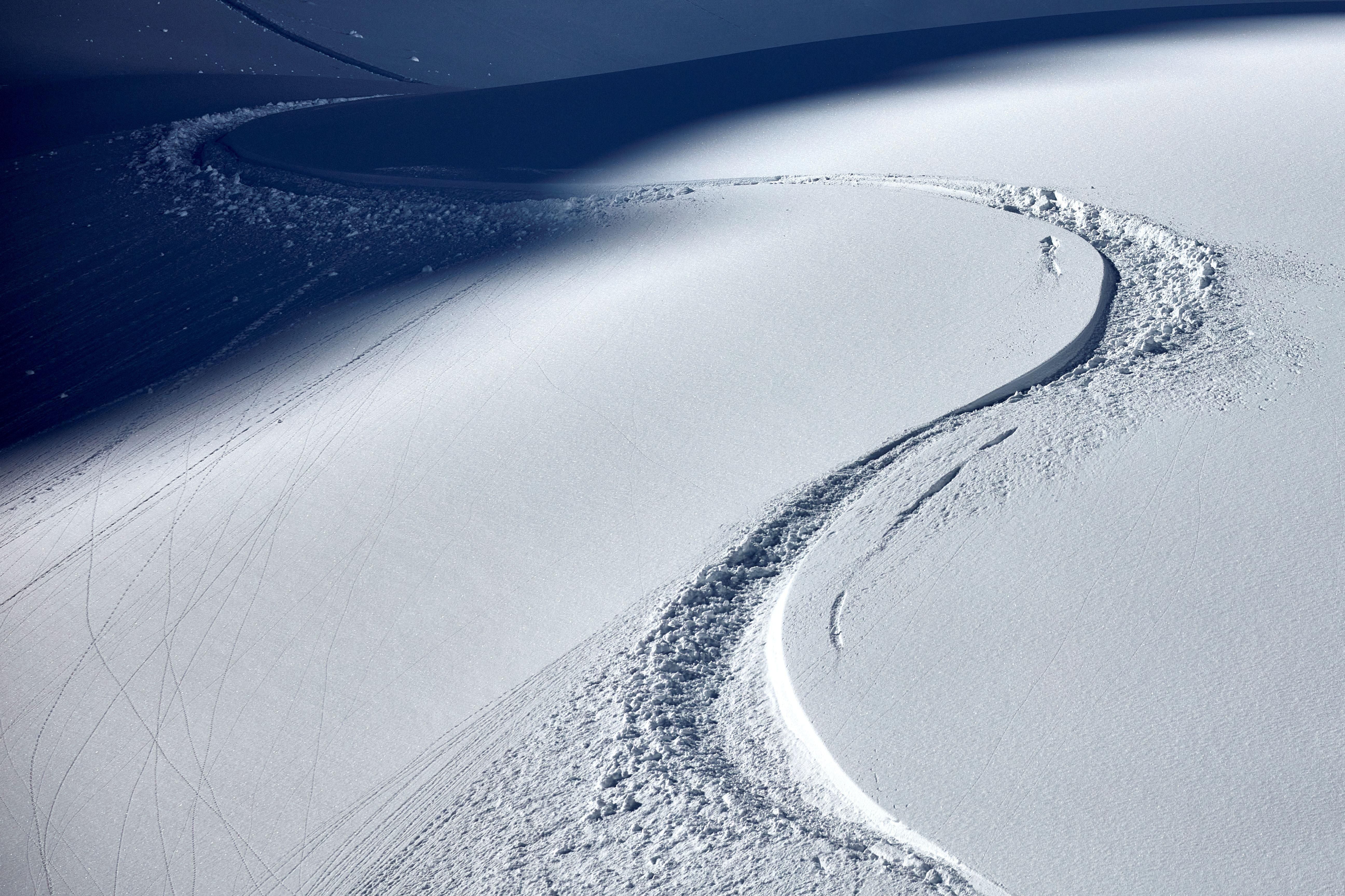 Ein verschneiter Hang mit klaren Spuren im Schnee. Die sanften Kurven zeigen die Bewegung eines Skifahrers.