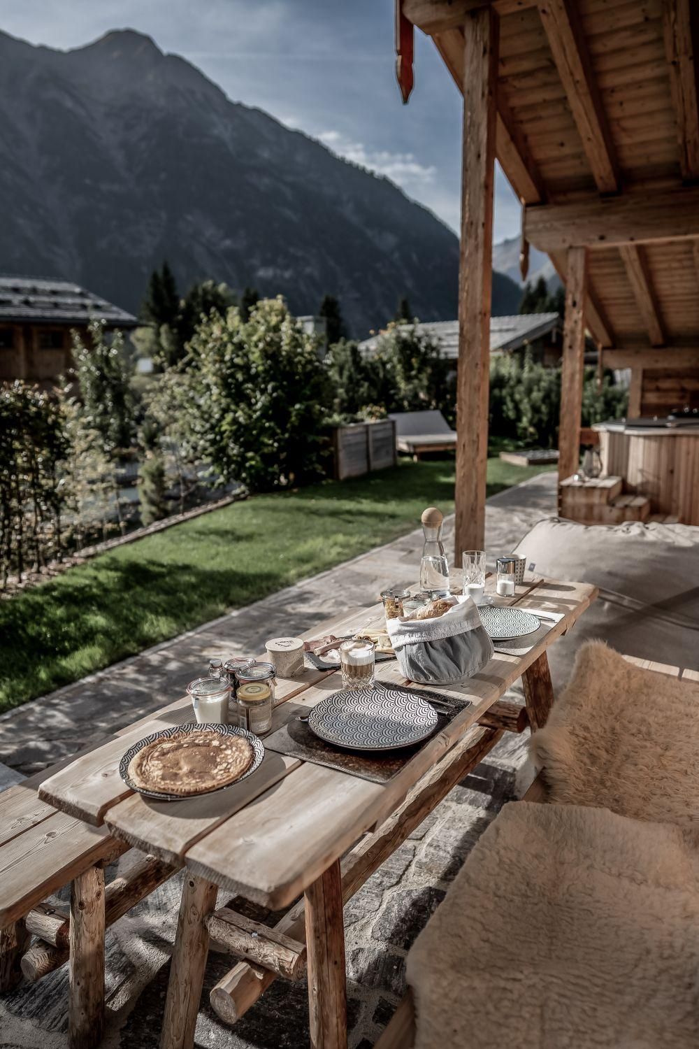 Ein gedeckter Tisch im Freien mit Bergen im Hintergrund. Die Atmosphäre ist gemütlich und einladend, ideal für ein Frühstück im Grünen.