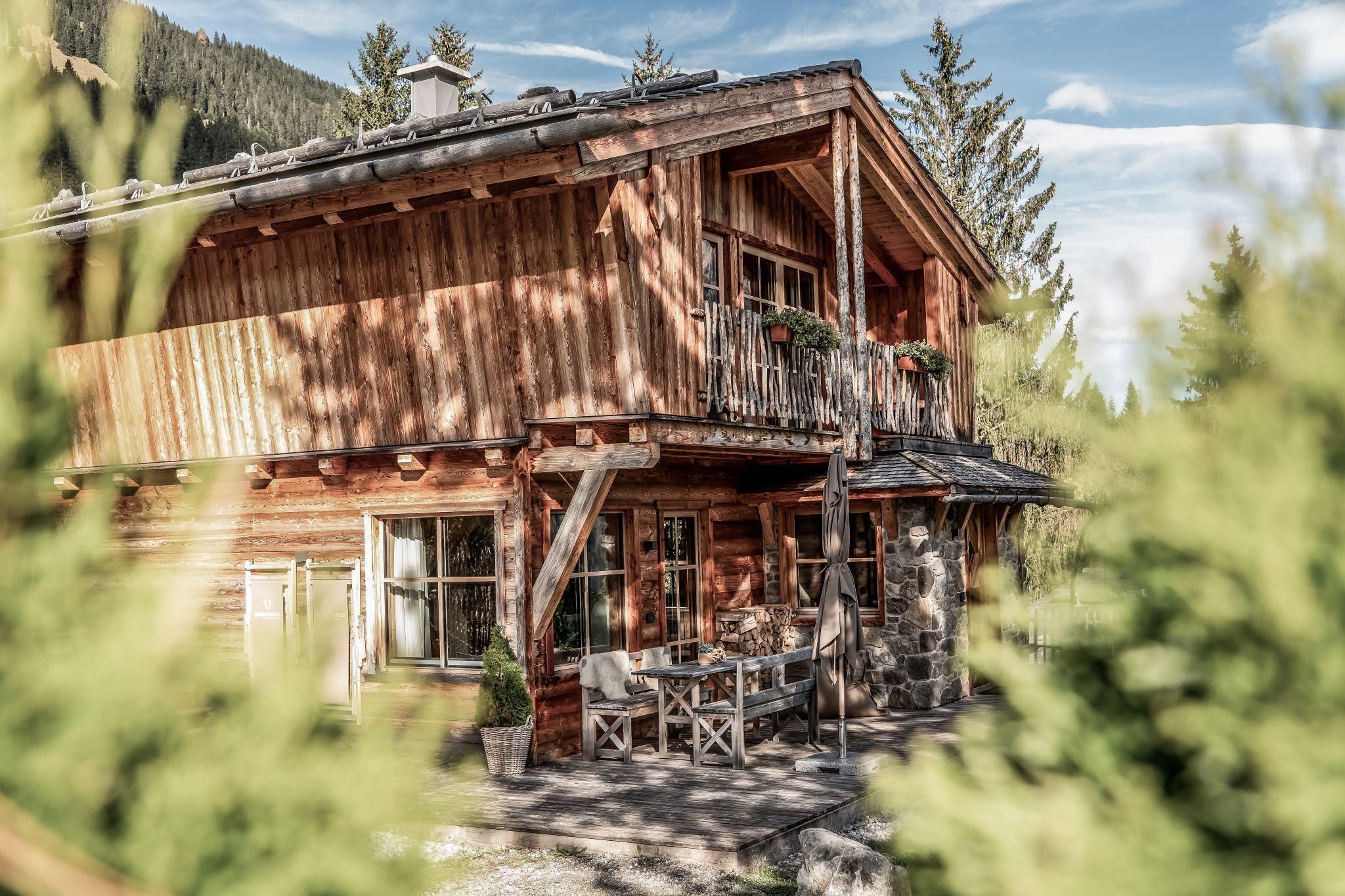 Ein schönes Chalet umgeben von Bäumen und einer malerischen Landschaft. Auf der Terrasse stehen Tische und Stühle, ideal für entspannte Tage im Freien.