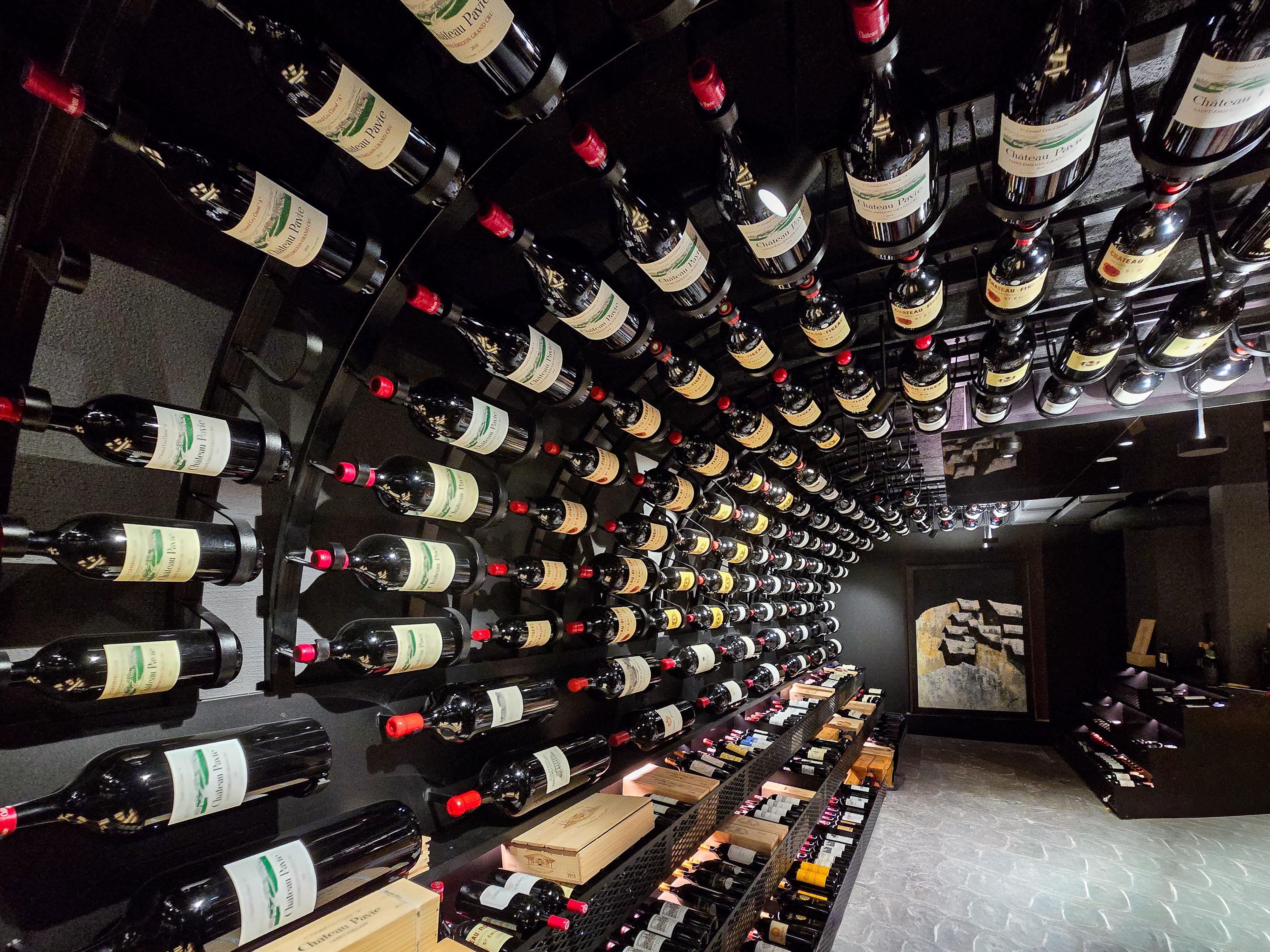 Ein Weinkeller mit vielen Flaschen Rotwein, die an einer runden Wand hängen. Die Atmosphäre ist elegant und einladend.