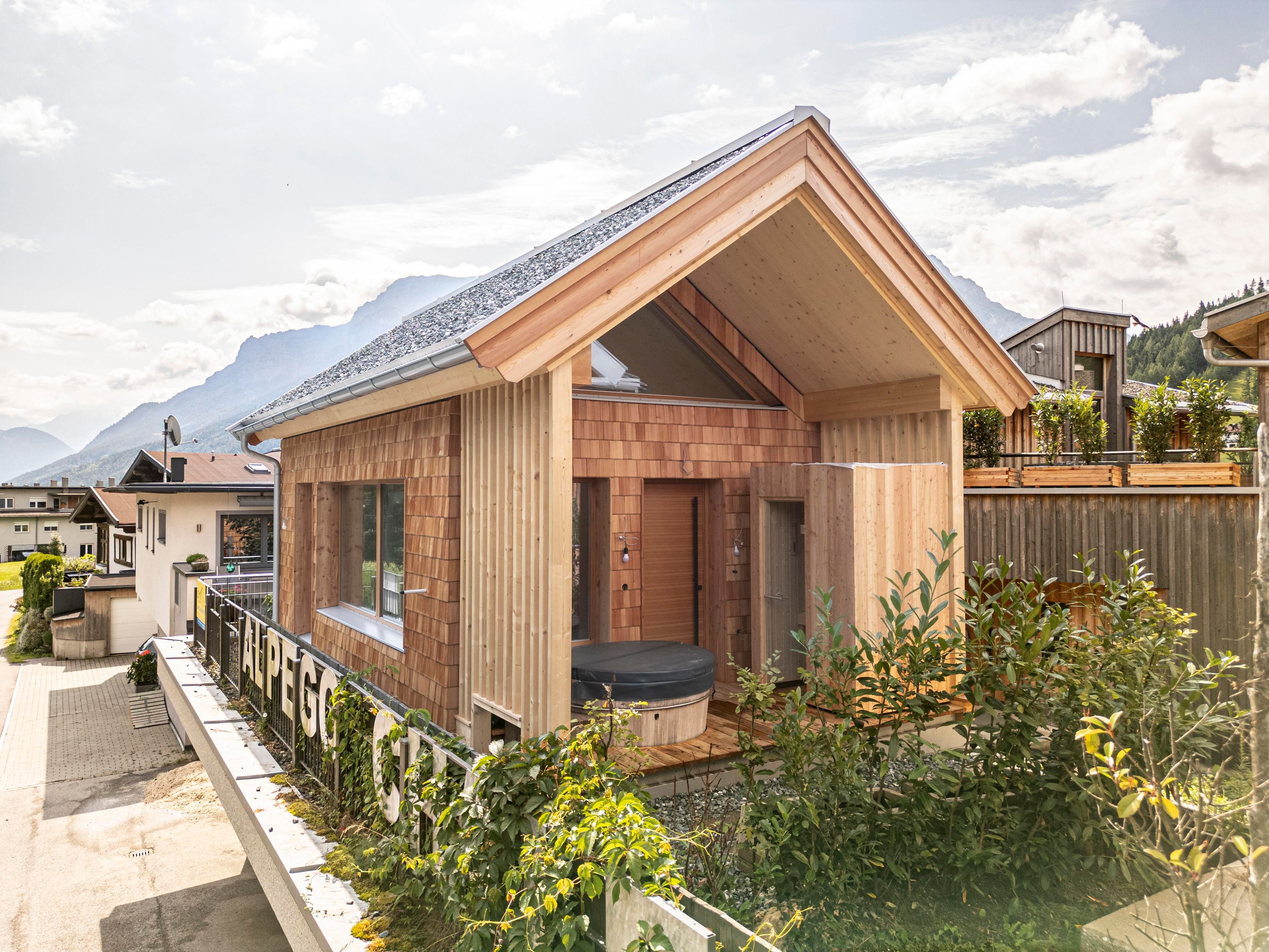 Ein modernes Holzhaus mit einer markanten Dachform. Umgeben von Pflanzen und einer malerischen Berglandschaft.