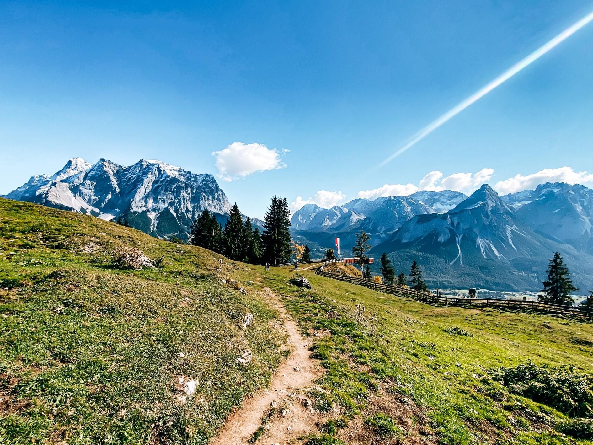 Eine malerische Berglandschaft mit grünen Wiesen und hohen Bergen im Hintergrund. Der Himmel ist klar und blau.