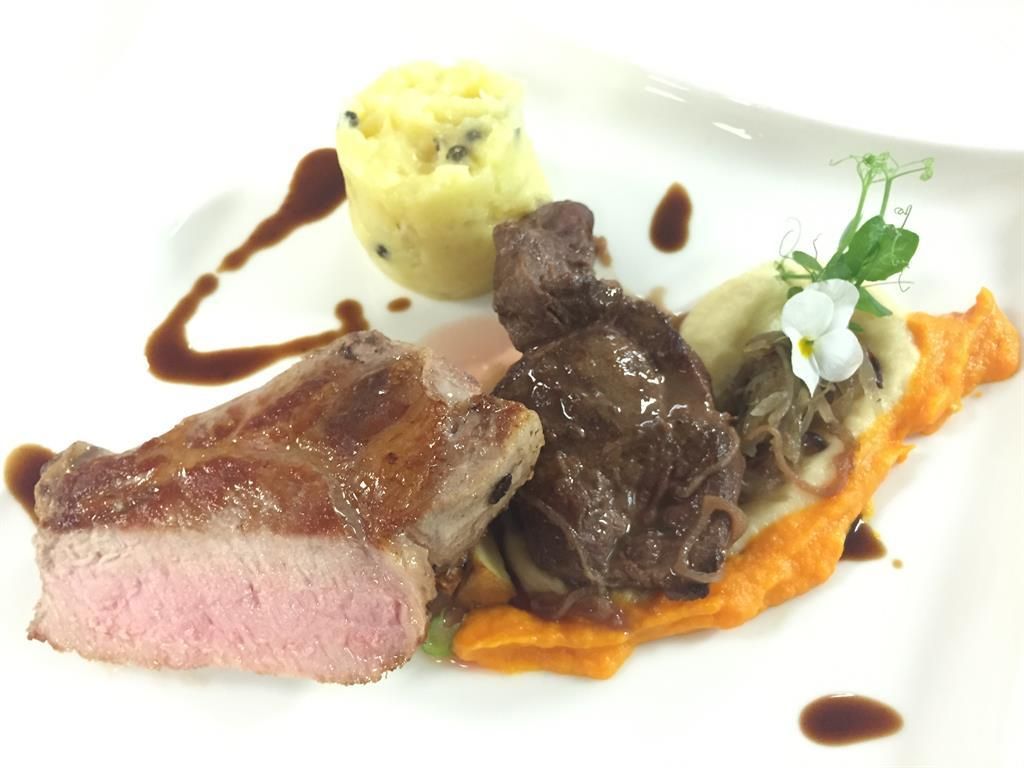 Ein kunstvoll angerichteter Teller mit saftigem Fleisch, pürierten Beilagen und einer Sauce. Das Gericht wird von einer kleinen Blume und frischen Kräutern garniert.