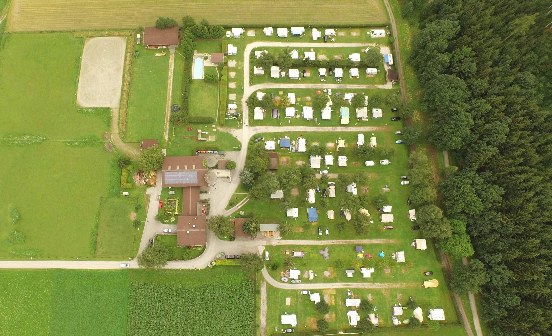Ein Übersichtsfoto eines Campingplatzes mit vielen Zelten und Wohnmobilen. Umgeben von grünen Wiesen und Bäumen.