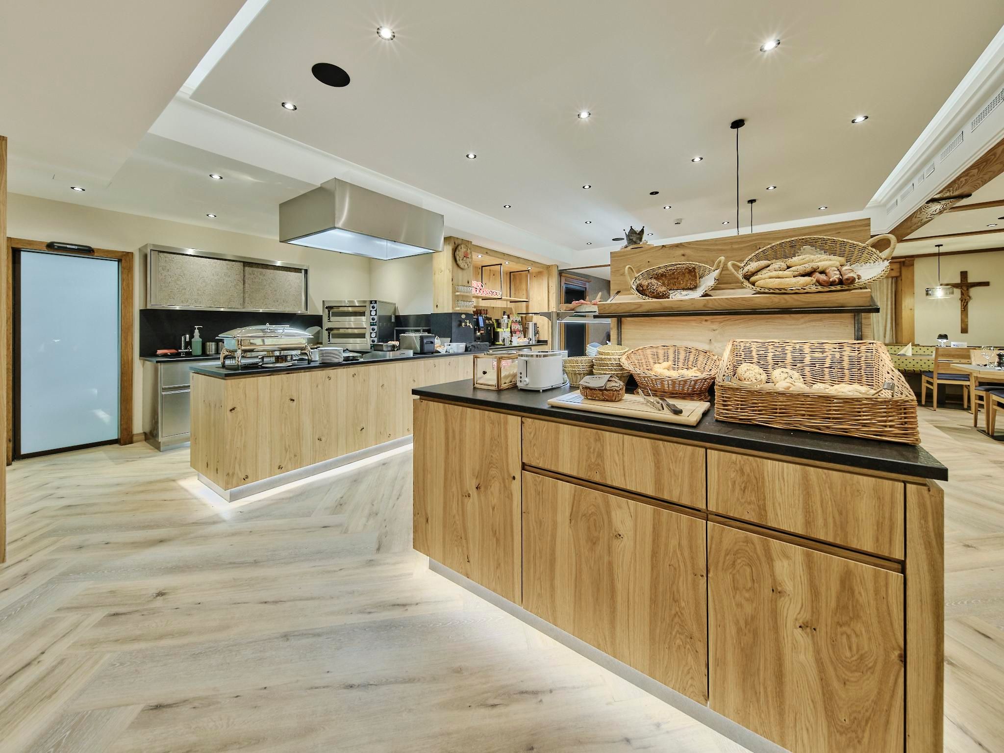 Ein modernes Restaurant mit hellen Holzregalen und einer offenen Küche. Auf der Anrichte sind frisch gebackenes Brot und andere Speisen angerichtet.