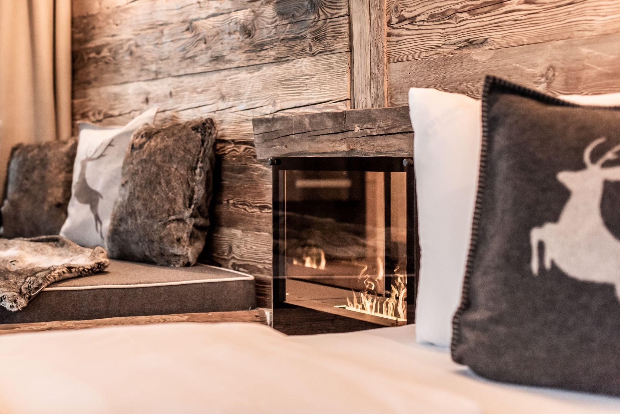 Ein gemütlicher Raum mit einer Holzwand, einer Couch und Kissen. Neben der Couch steht ein moderner Kamin, der Wärme und Gemütlichkeit ausstrahlt.
