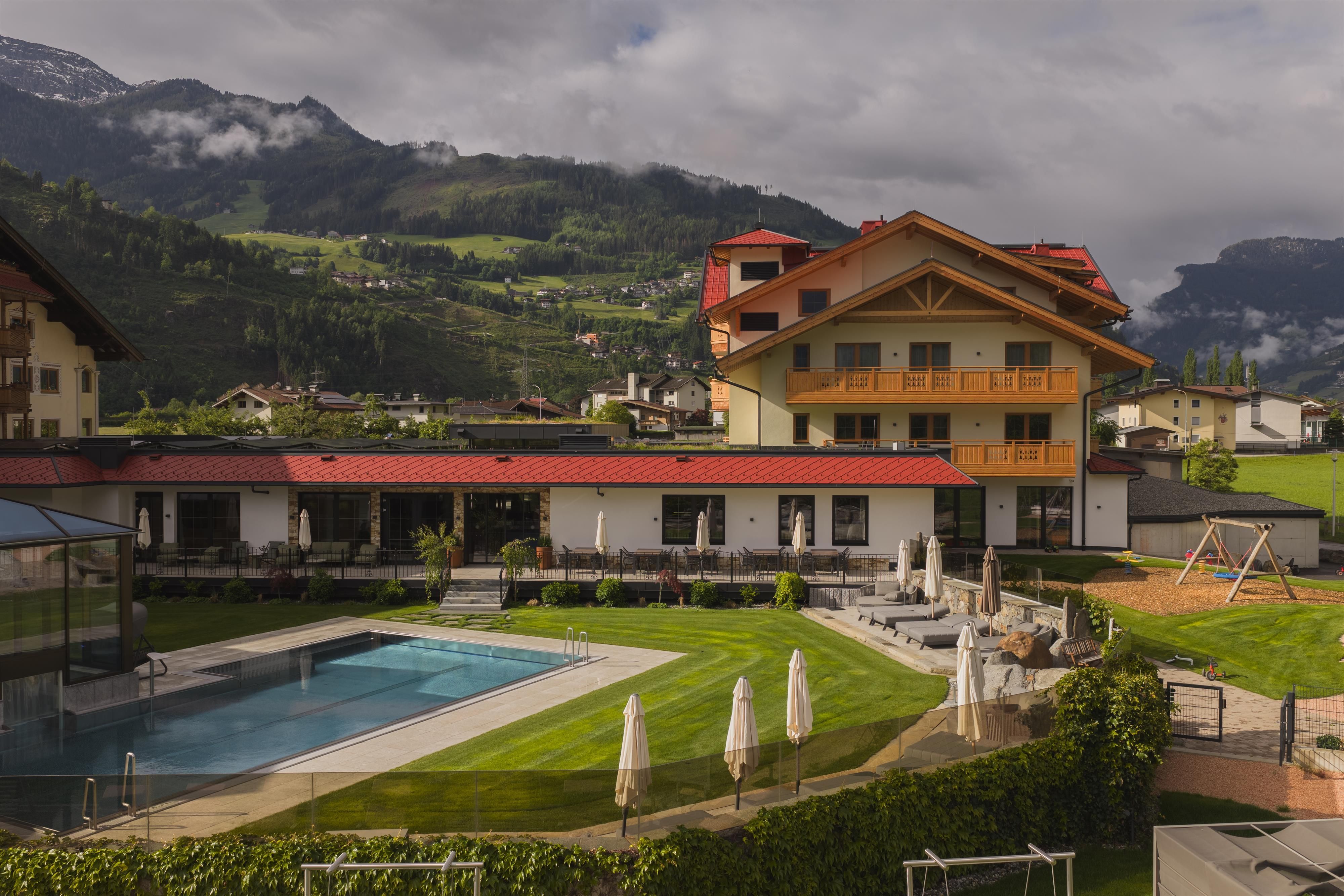 Ein Hotel mit schöner Architektur und einem Außenpool. Die Umgebung ist grün und von Bergen umgeben.