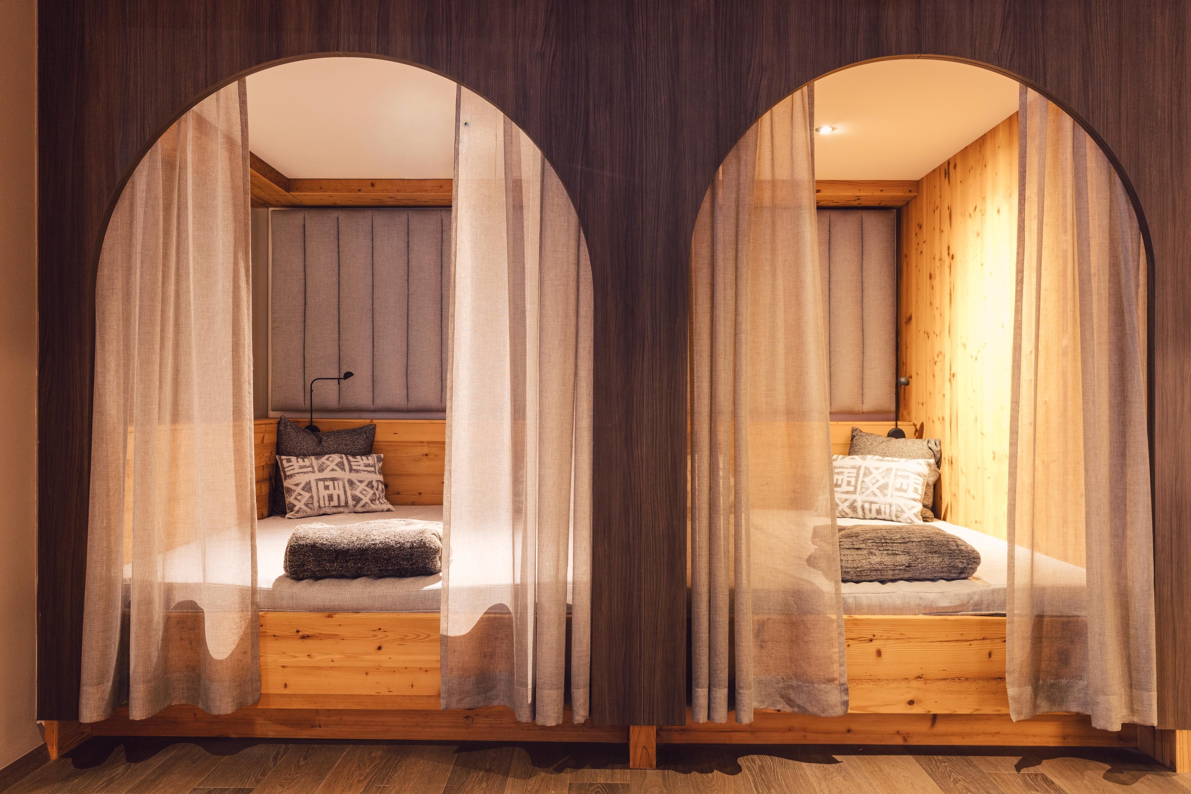 Zwei komfortable Betten in einem modernen Raum mit Holzverkleidung. Die Betten sind durch halbtransparente Vorhänge voneinander getrennt.