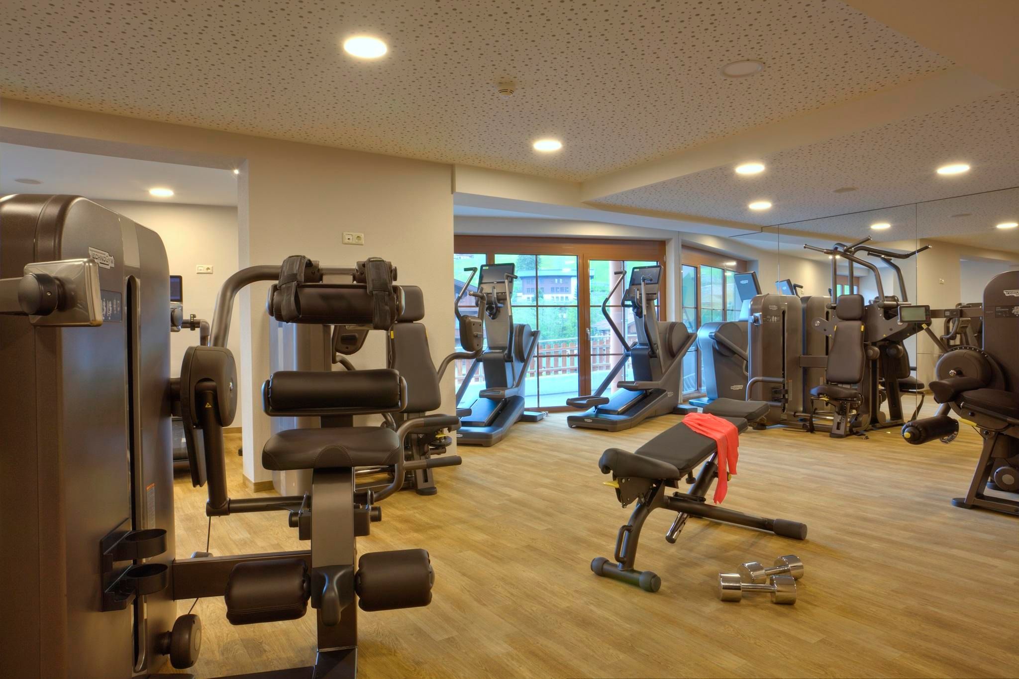 Ein gut ausgestatteter Fitnessraum mit verschiedenen Geräten. Große Fenster lassen viel Licht herein.