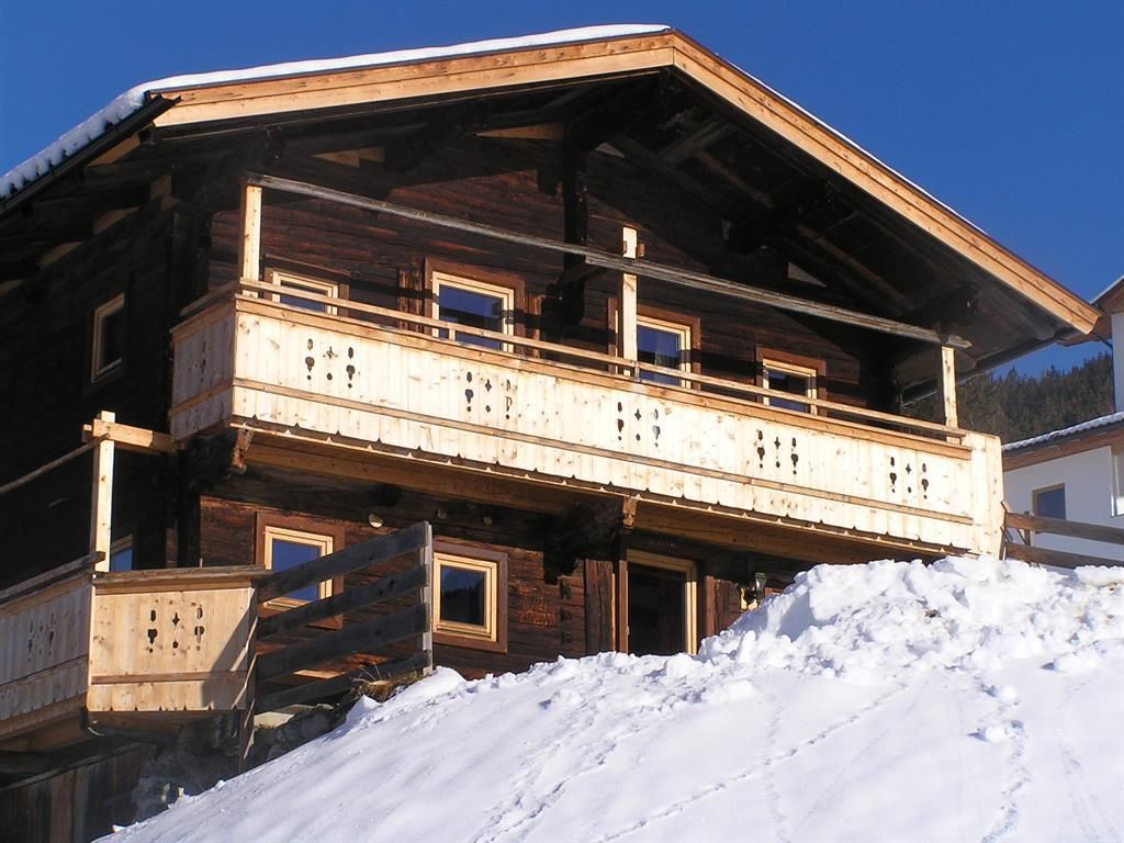 Ein charmantes Holzhaus mit einem Balkon, umgeben von Schnee. Der klare blaue Himmel sorgt für eine winterliche Atmosphäre.