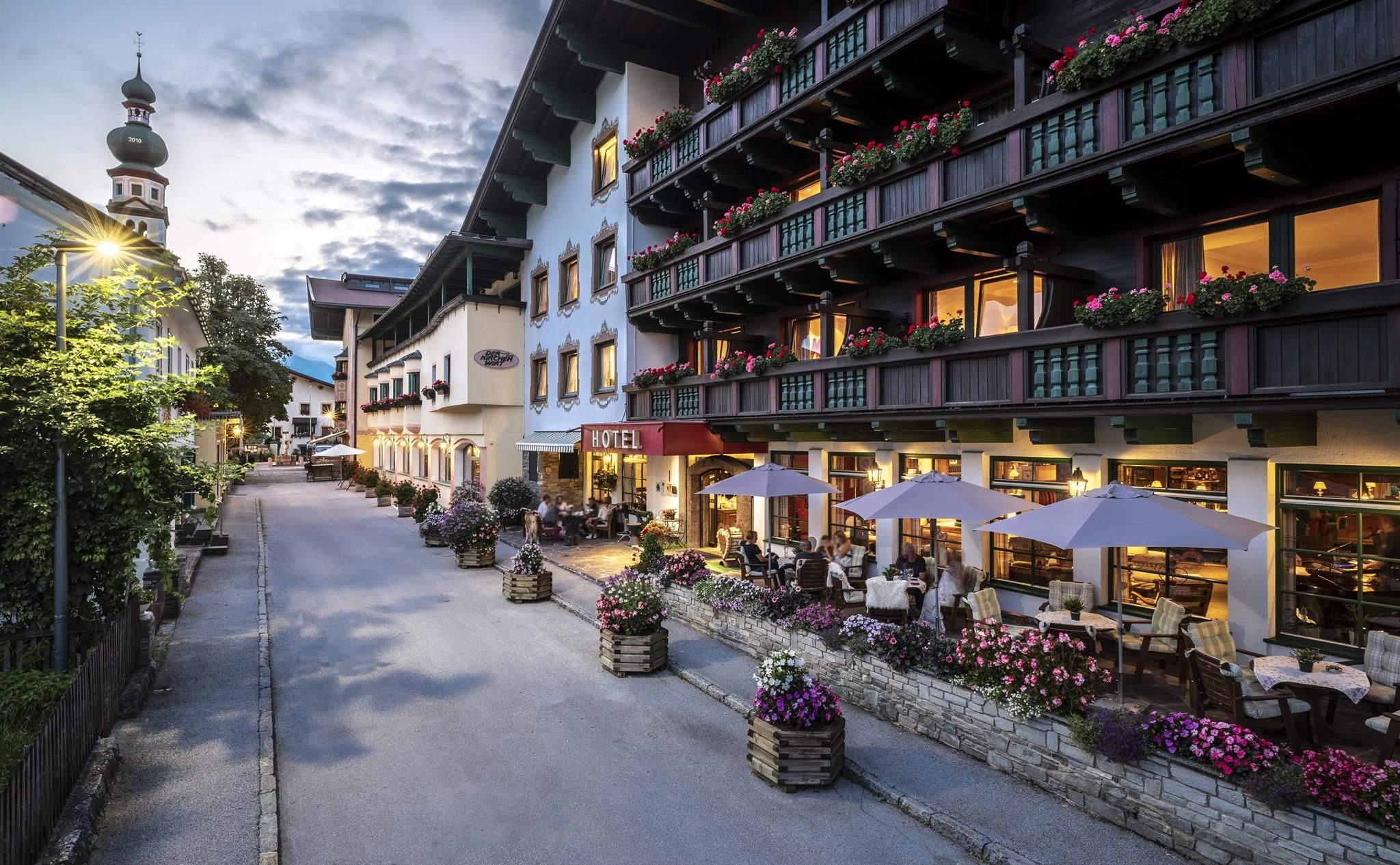 Ein charmantes Hotel in einer malerischen Straße, umgeben von blühenden Pflanzen. Die Terrasse lädt zum Verweilen ein und die Architektur zeigt alpine Eleganz.