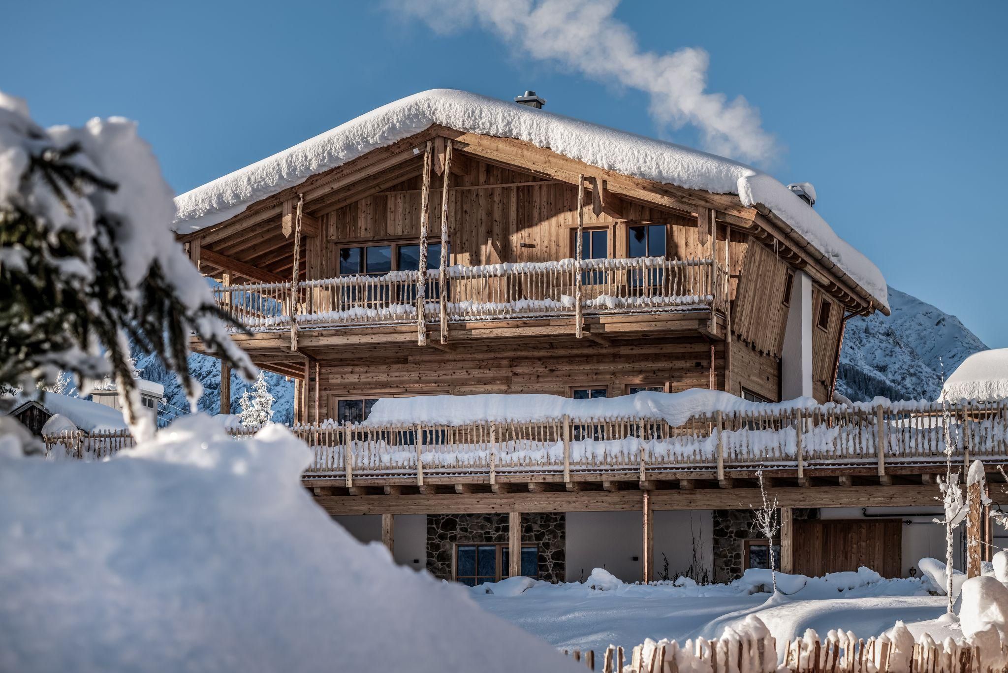 Ein schönes Chalet im Winter mit schneebedecktem Dach und Holzverkleidung. Die Umgebung ist von weißem Schnee und blauen Himmel geprägt.