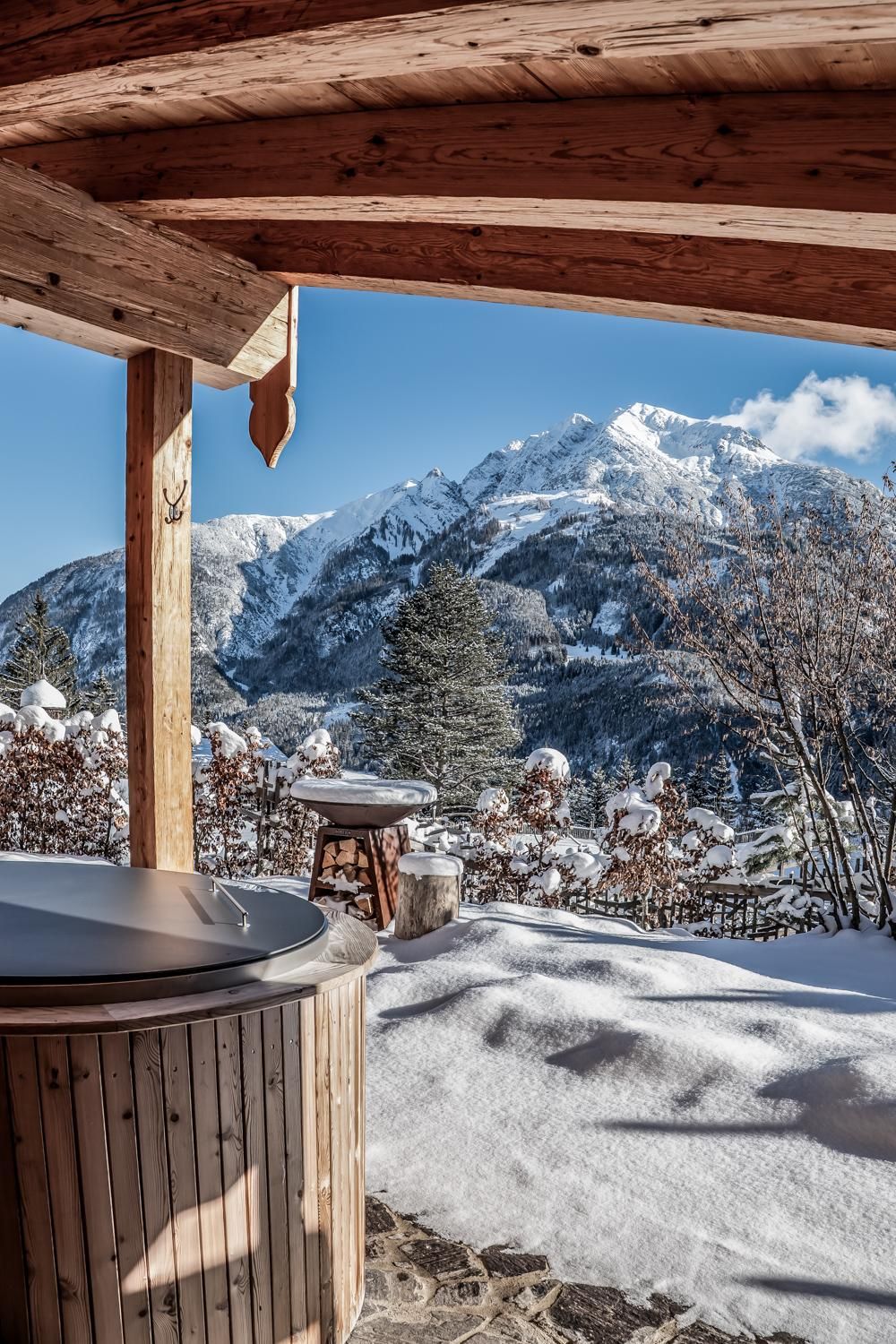 Ein gemütlicher Outdoor-Bereich mit Blick auf schneebedeckte Berge. Der Boden ist mit frischem Schnee bedeckt und die Sonne scheint am klaren Himmel.