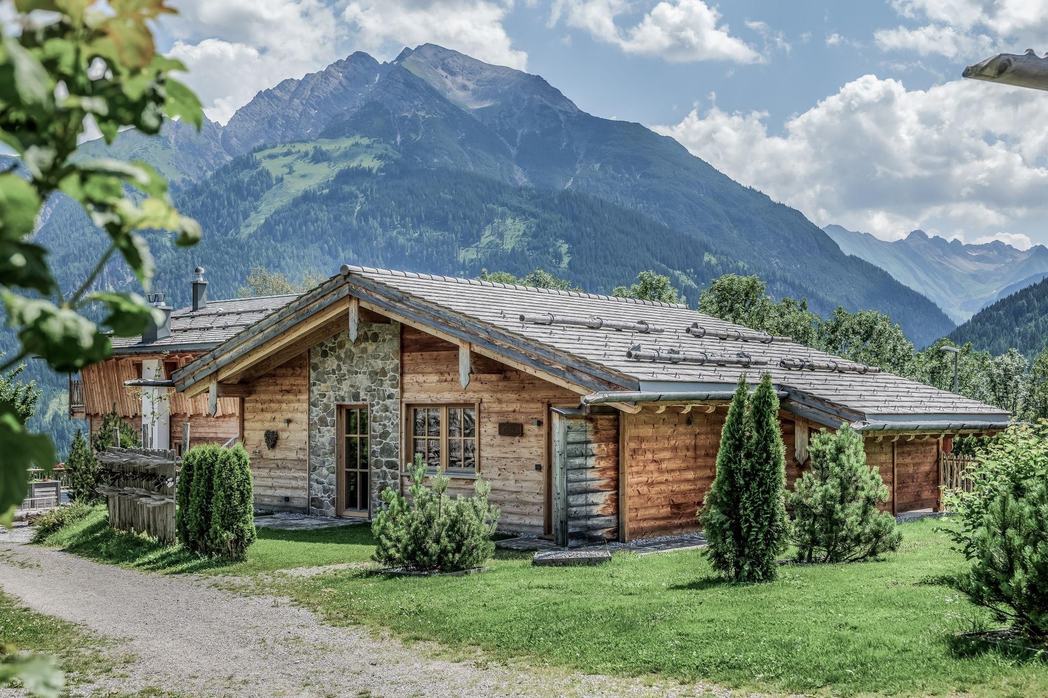 Eine gemütliche Chalet umgeben von grünen Wiesen und Bergen. Der Himmel ist teilweise bewölkt und die Landschaft wirkt friedlich.