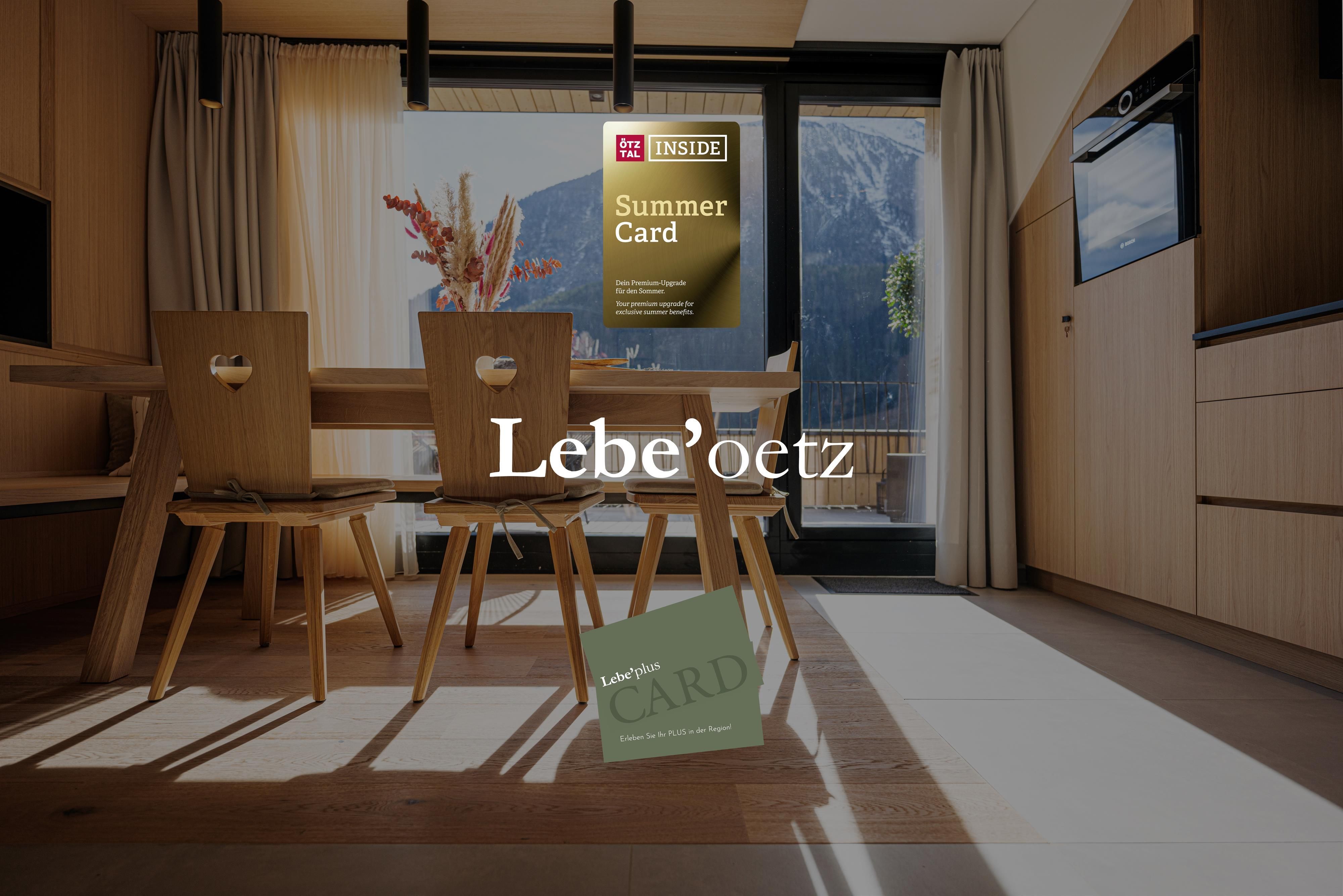 Ein modernes und helles Wohnzimmer mit Holzstühlen und einem Tisch. Im Hintergrund sind Fenster und eine Karte zu sehen, die auf Sommeraktivitäten hinweist.