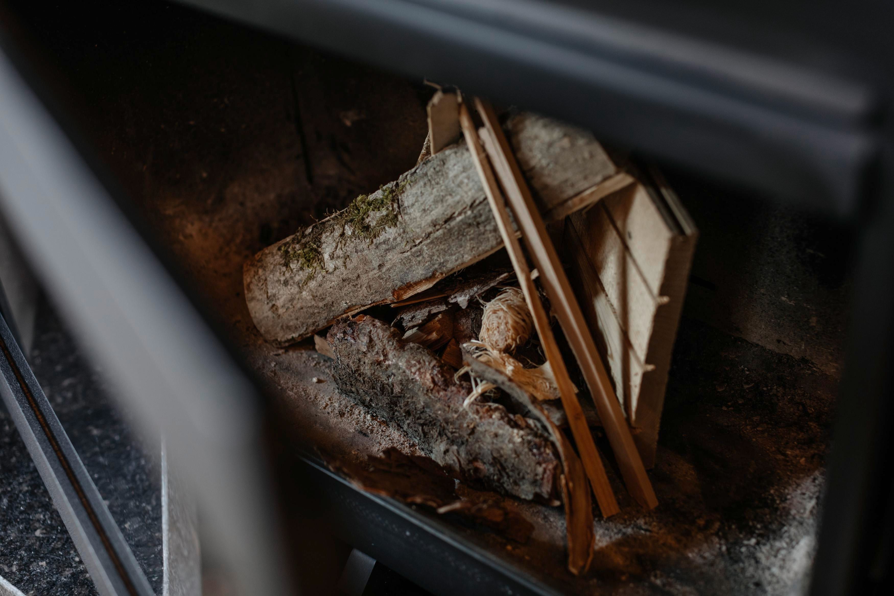 Ein Kamin mit Holzscheiten und feinen Ästen. Der Raum ist dunkel und die Umgebung scheint gemütlich zu sein.