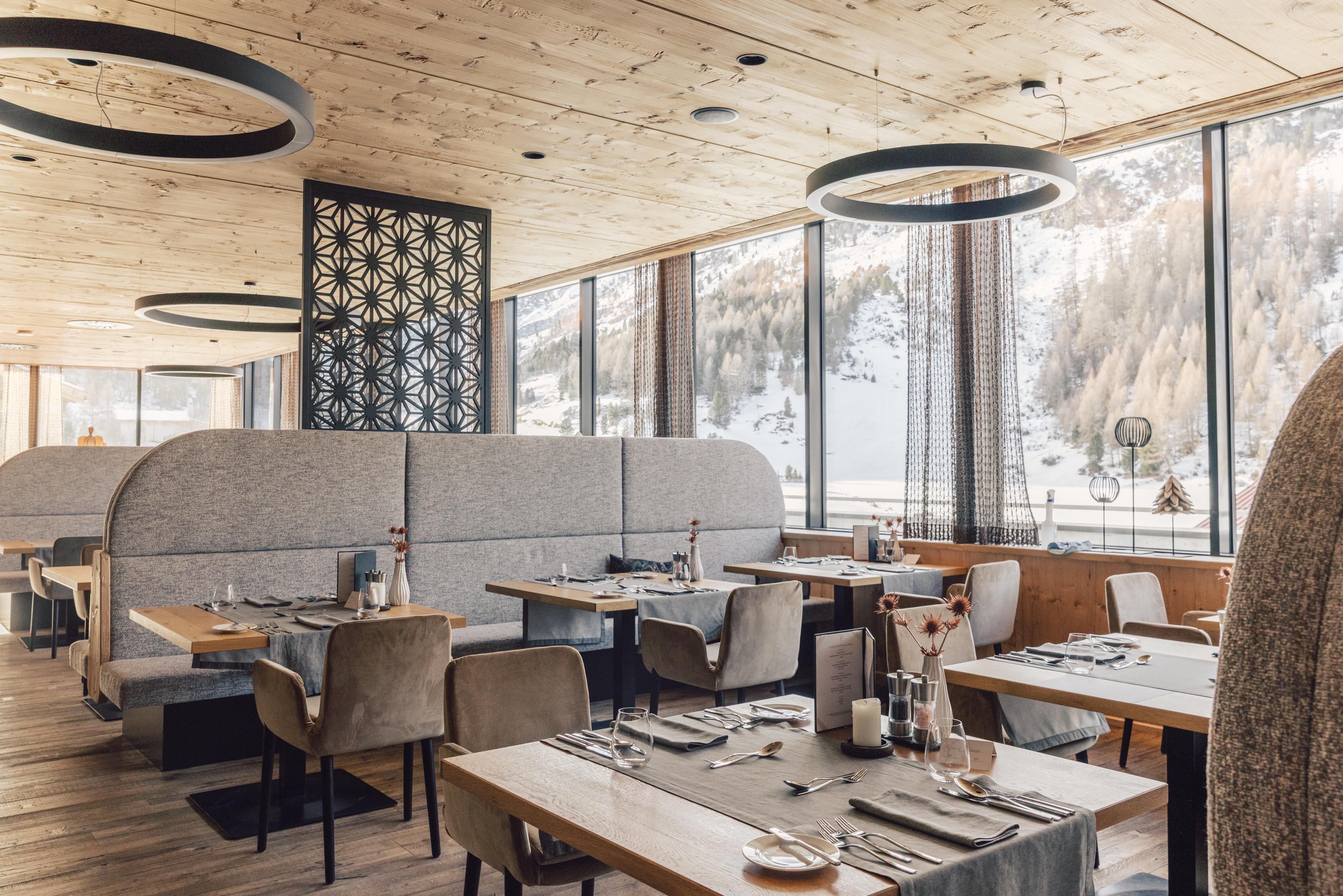 Ein modernes Restaurant mit gemütlichen Sitzecken und großen Fenstern. Der Raum ist hell und einladend, mit einem schönen Blick auf die winterliche Landschaft.