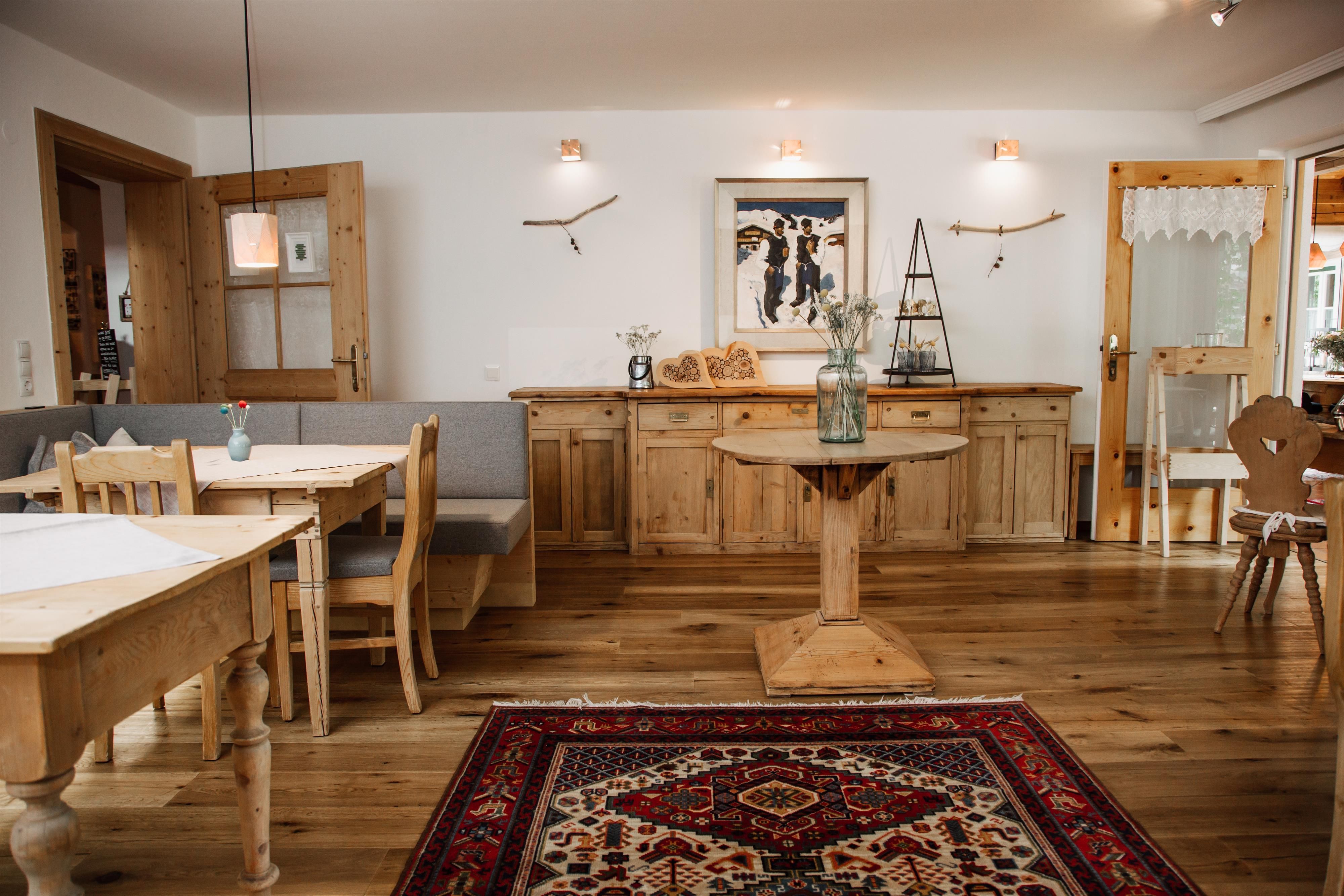 Ein stilvoll eingerichteter Raum mit Holzmöbeln und einem Teppich. Die Wände sind hell, und es gibt ein Kunstwerk sowie natürliche Lichtquellen.