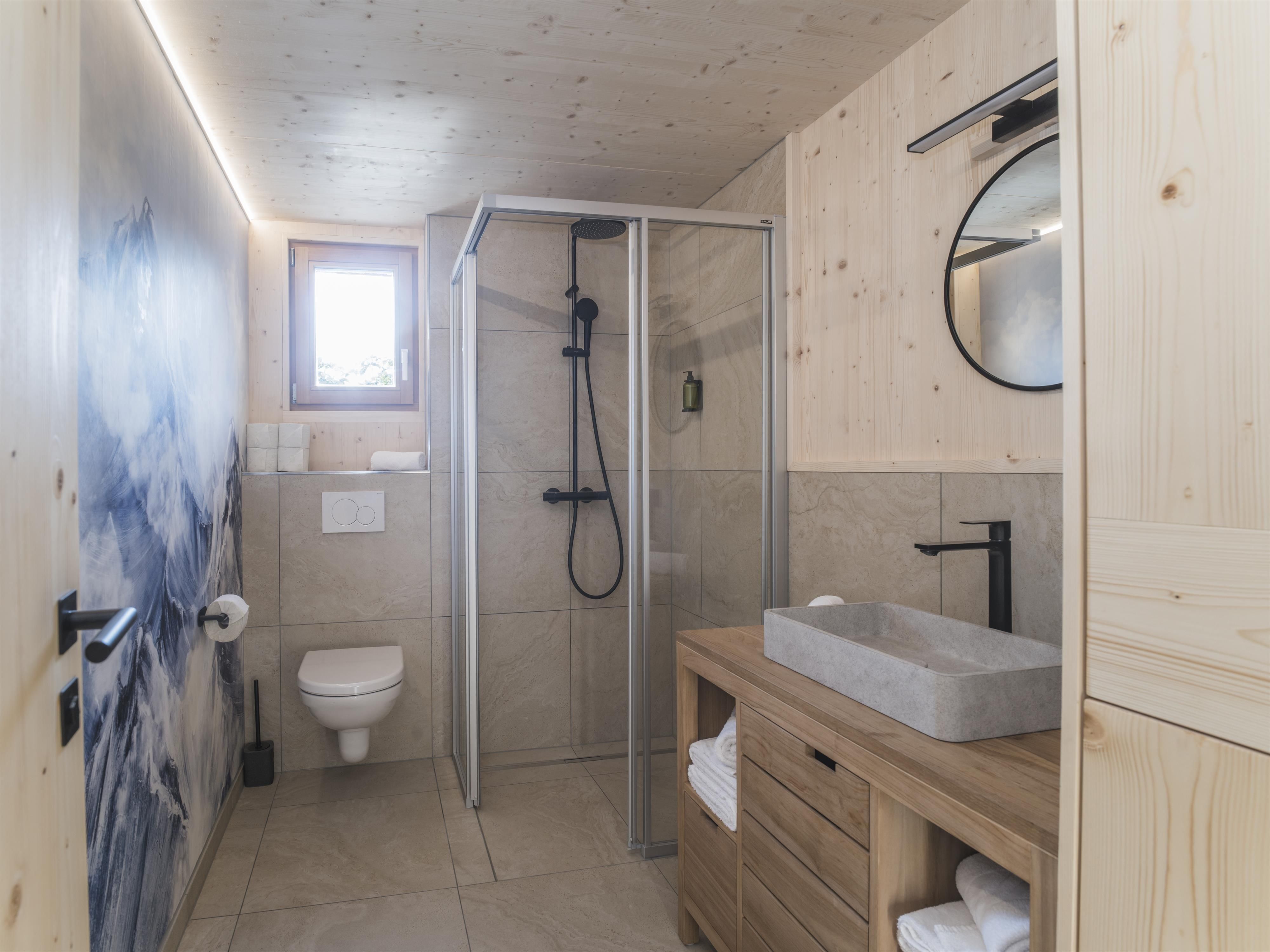 Ein modernes Badezimmer mit Holzverkleidung. Es zeigt eine Dusche, ein Waschbecken und eine Toilette in einem klaren, sauberen Design.