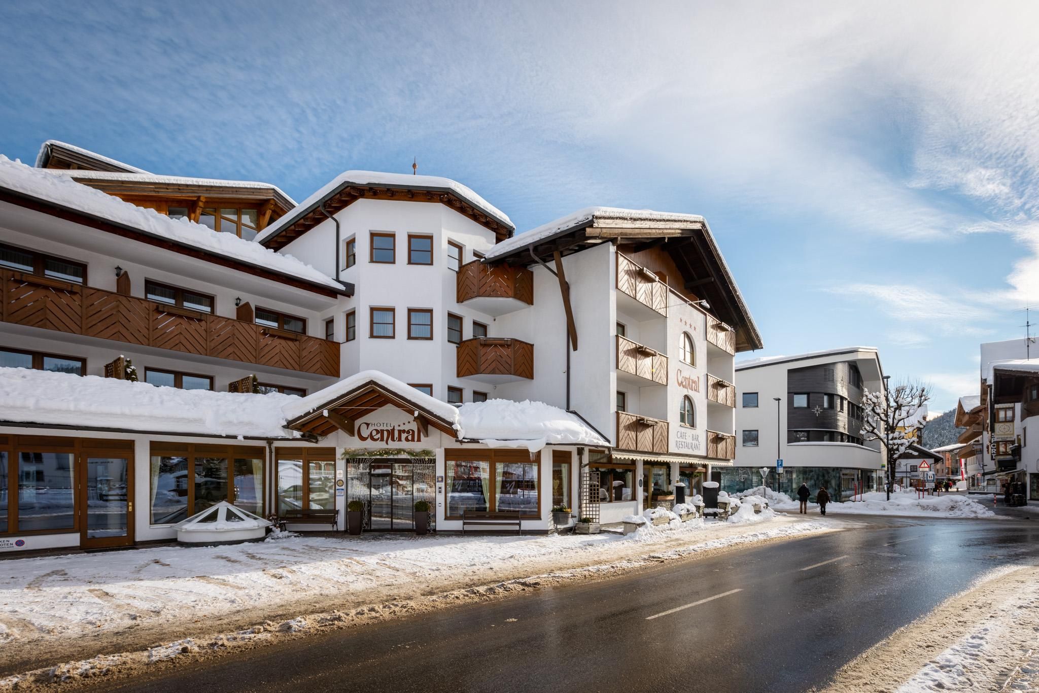 Ein charmantes Hotel in einer verschneiten Umgebung. Die Straße vor dem Hotel ist gut befahrbar und die Architektur wirkt einladend.